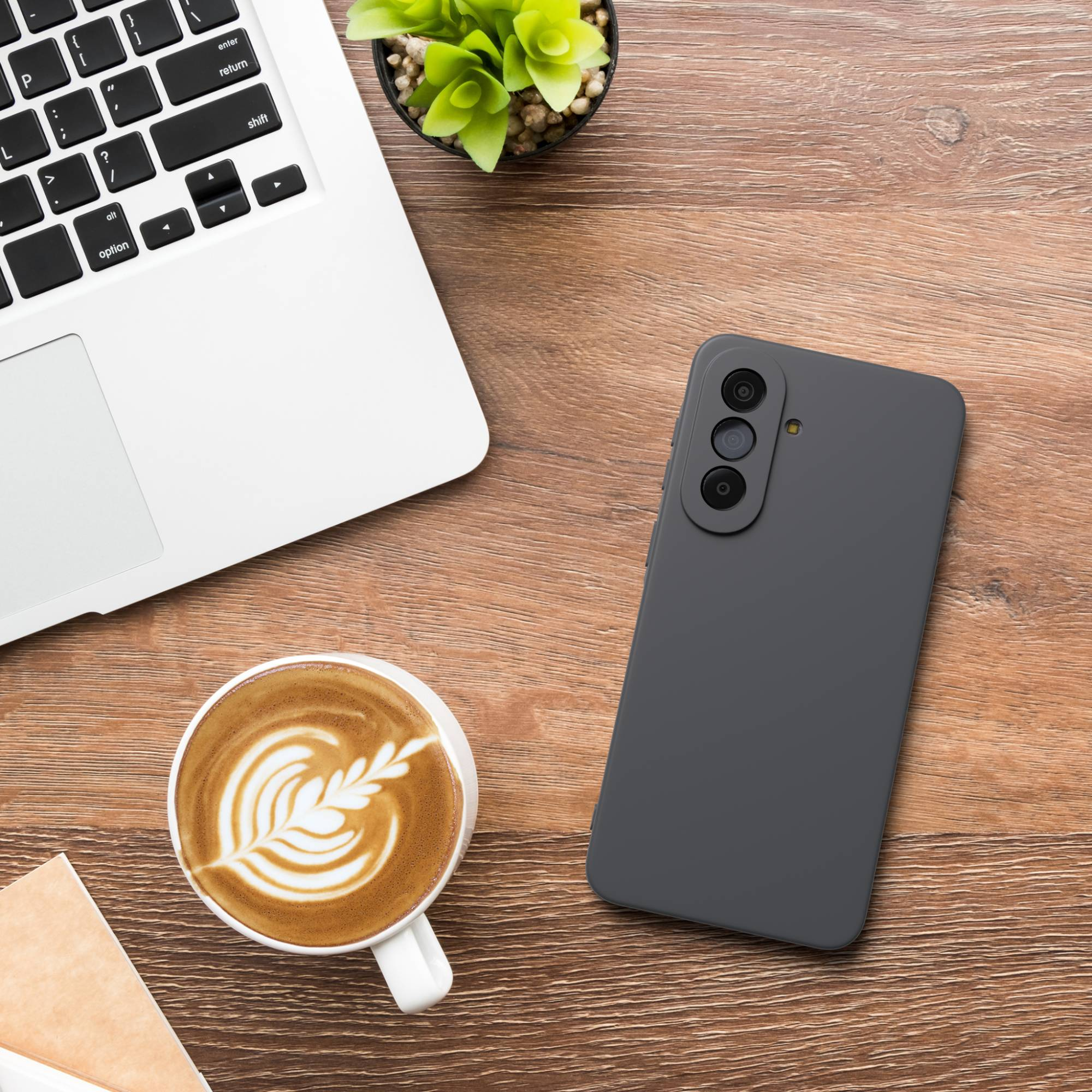 Ein Laptop, ein Handy, eine Kaffeetasse und eine Pflanze auf einem Holztisch.