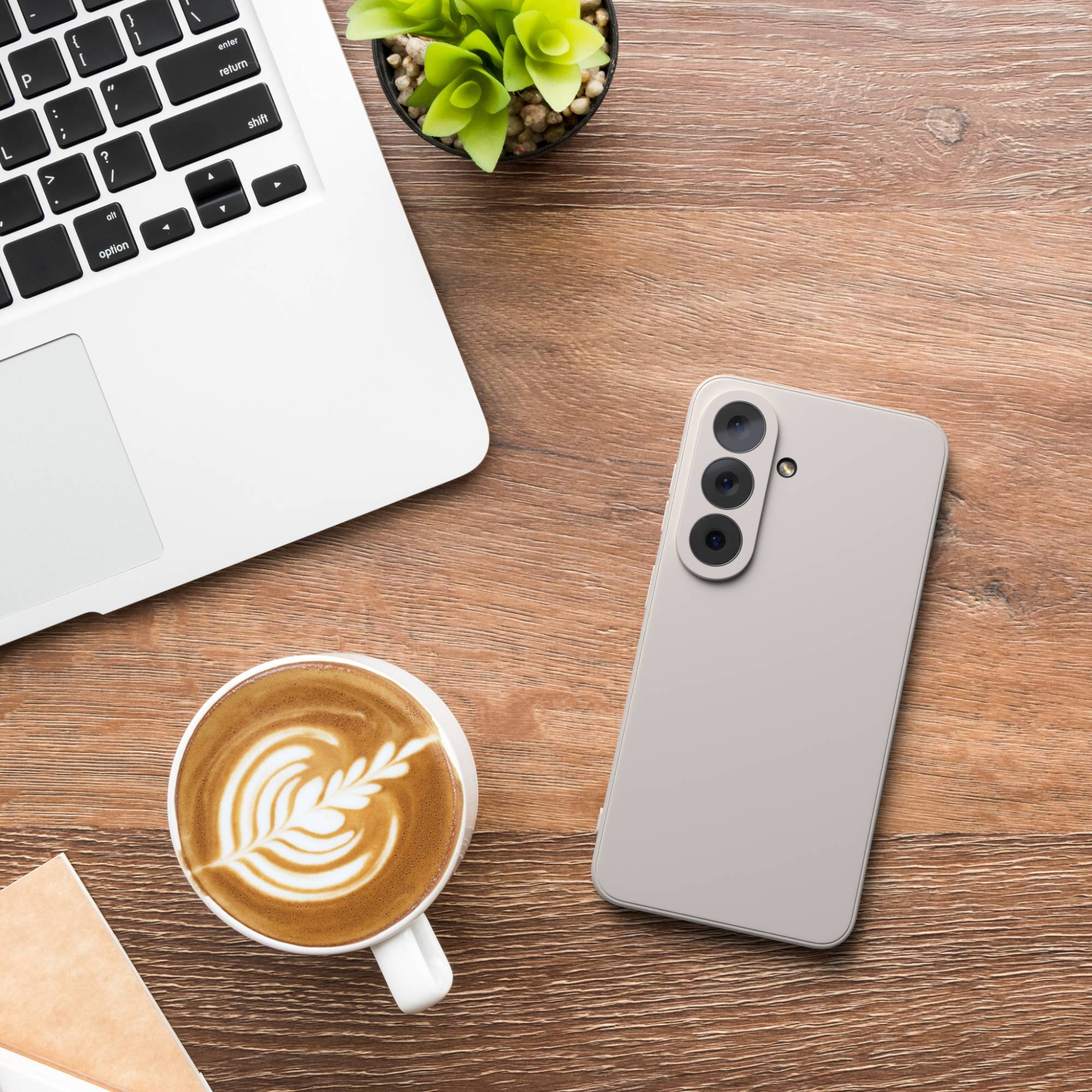 Ein Laptop, eine Kaffeetasse mit Latte Art und ein Smartphone liegen auf einem Holztisch.