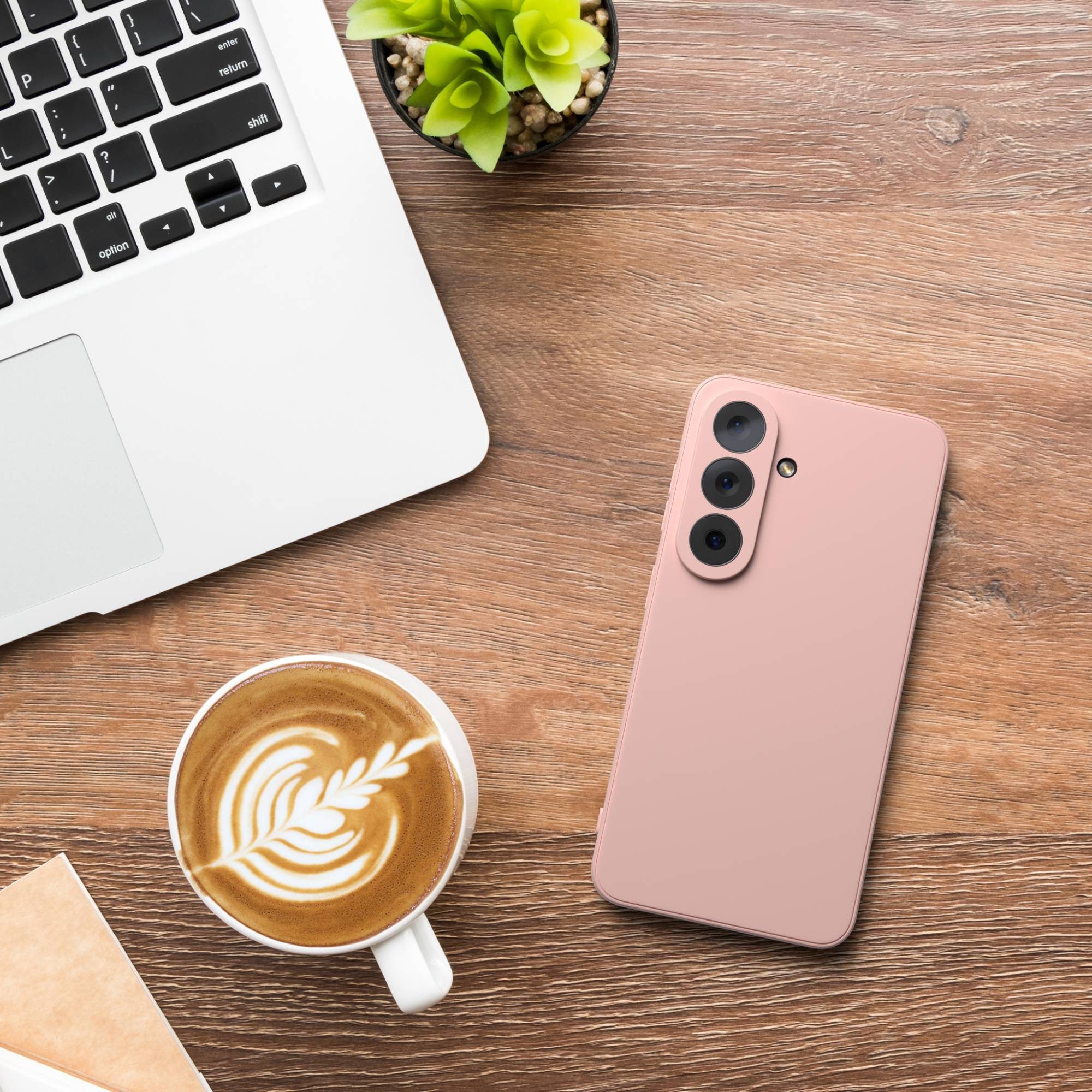 Ein rosafarbenes Smartphone, Kaffee, Laptop und Pflanze auf einem Holzschreibtisch.