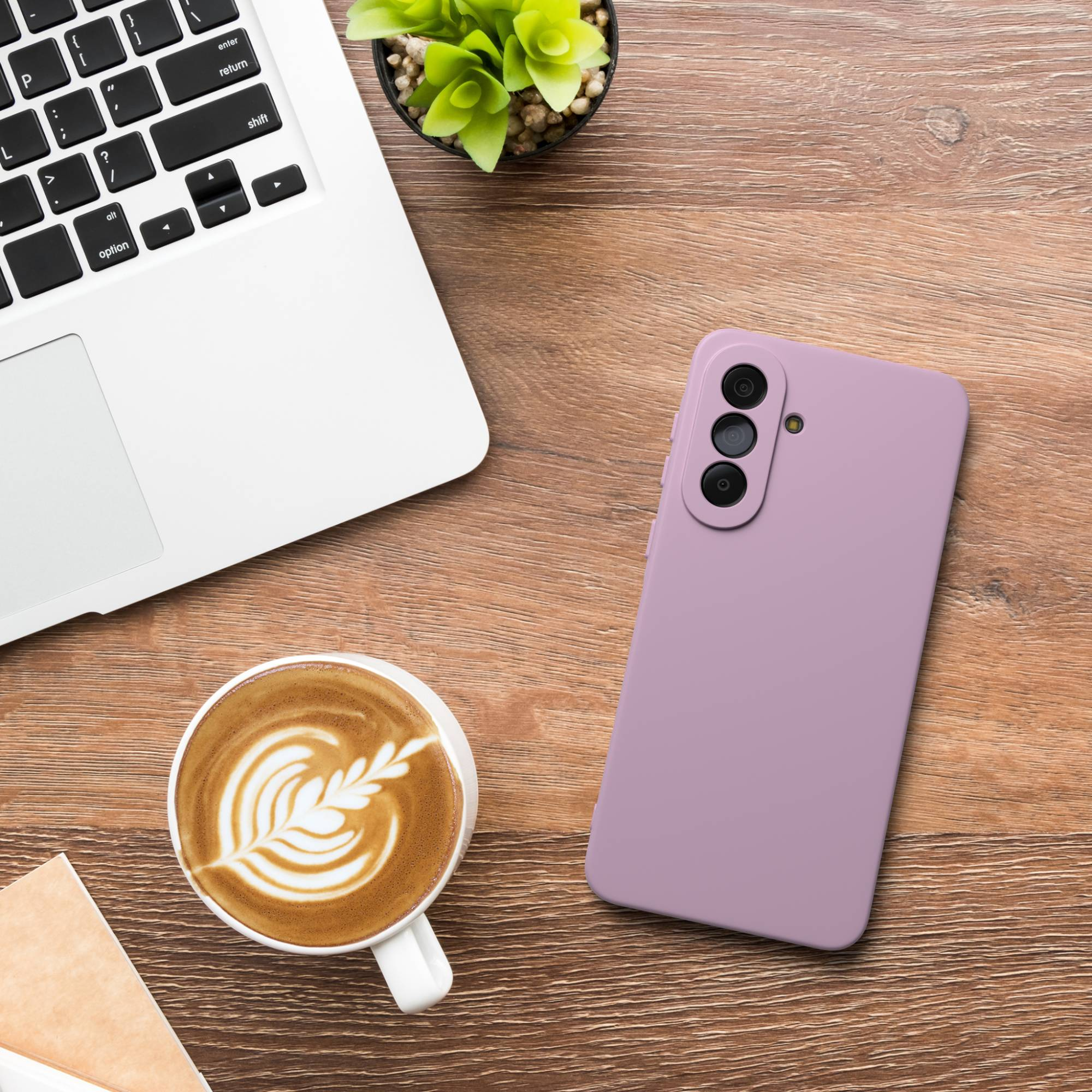 Ein Laptop, eine Kaffeetasse mit Latte Art und ein lila Handy auf einem Holztisch.