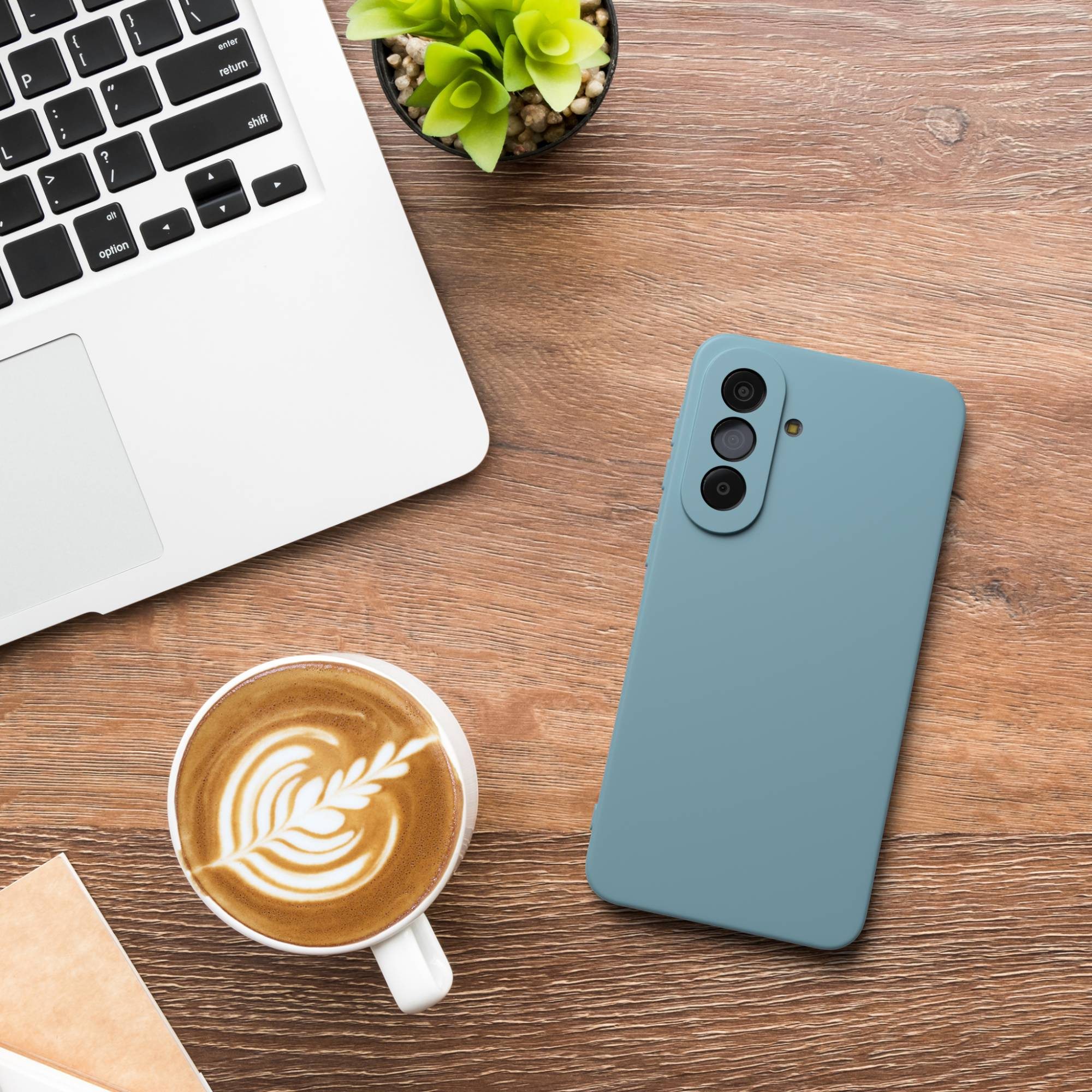 Ein Laptop, eine Kaffeetasse mit Latte Art und ein blaues Smartphone liegen auf einem Holztisch.