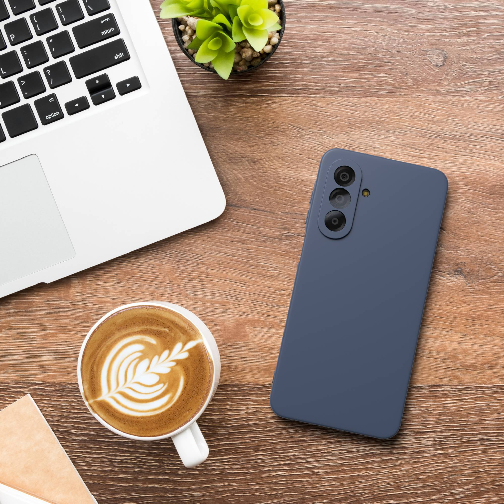 Ein Laptop, Kaffee mit Latte Art und ein blaues Handy auf einem Holzschreibtisch.