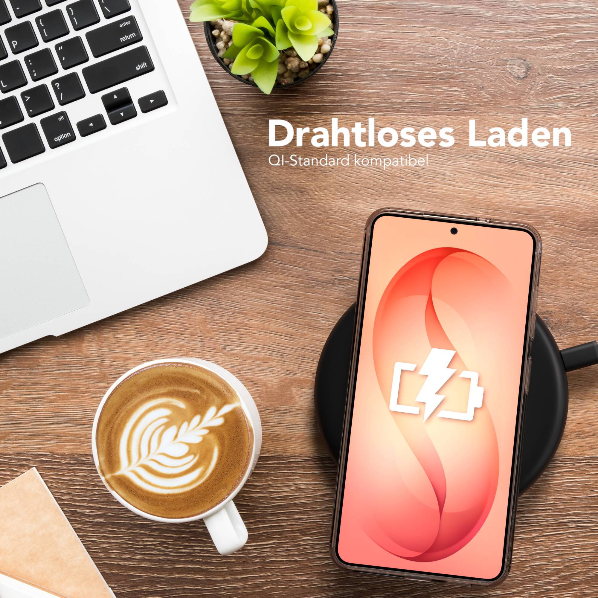 Ein Laptop, eine Kaffeetasse, ein Smartphone auf Ladegerät und eine Pflanze.