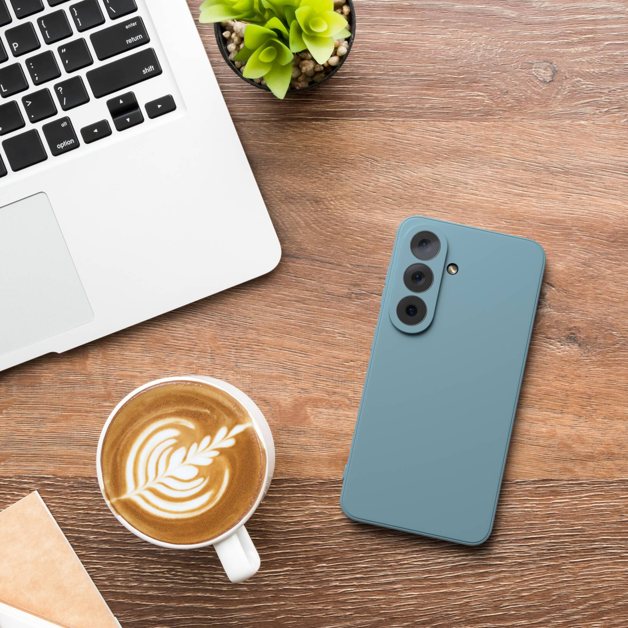 Ein Laptop, eine Kaffeetasse mit Latte Art und ein blaues Smartphone auf einem Holztisch.