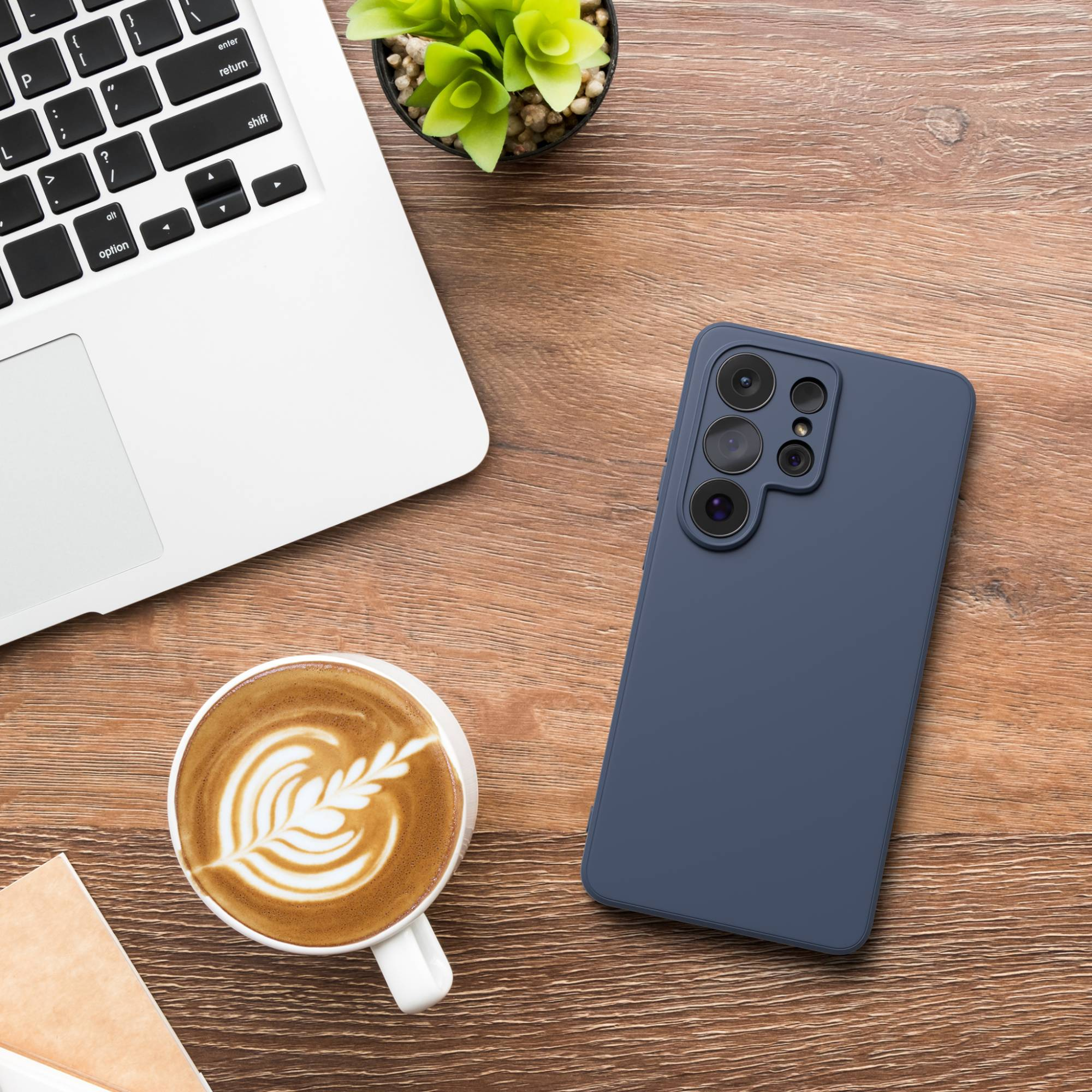 Dunkelblaues Handy neben Laptop, Kaffeetasse mit Latte Art und Pflanze.