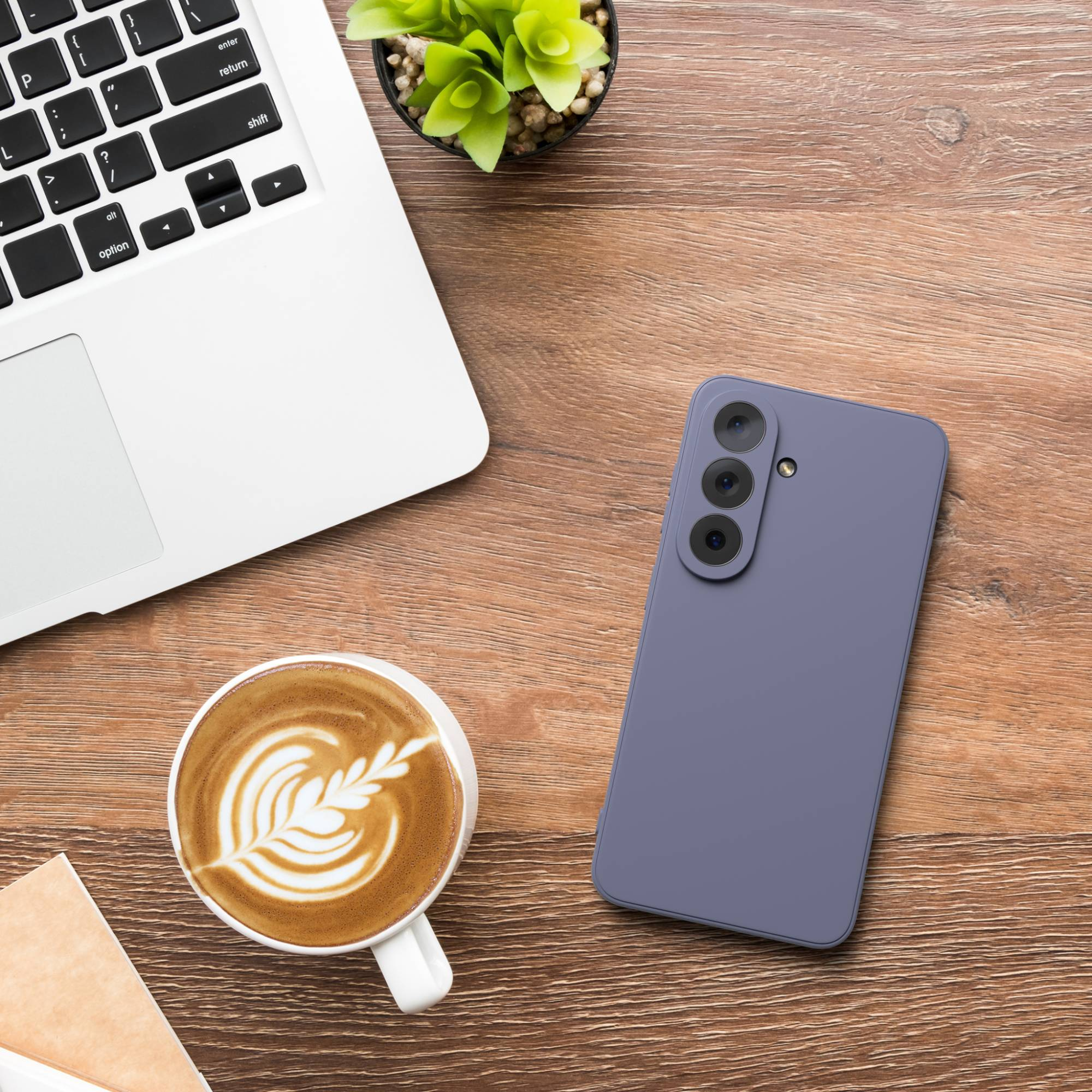 Ein Laptop, eine Kaffeetasse mit Latte Art und ein lila Smartphone liegen auf einem Holztisch.