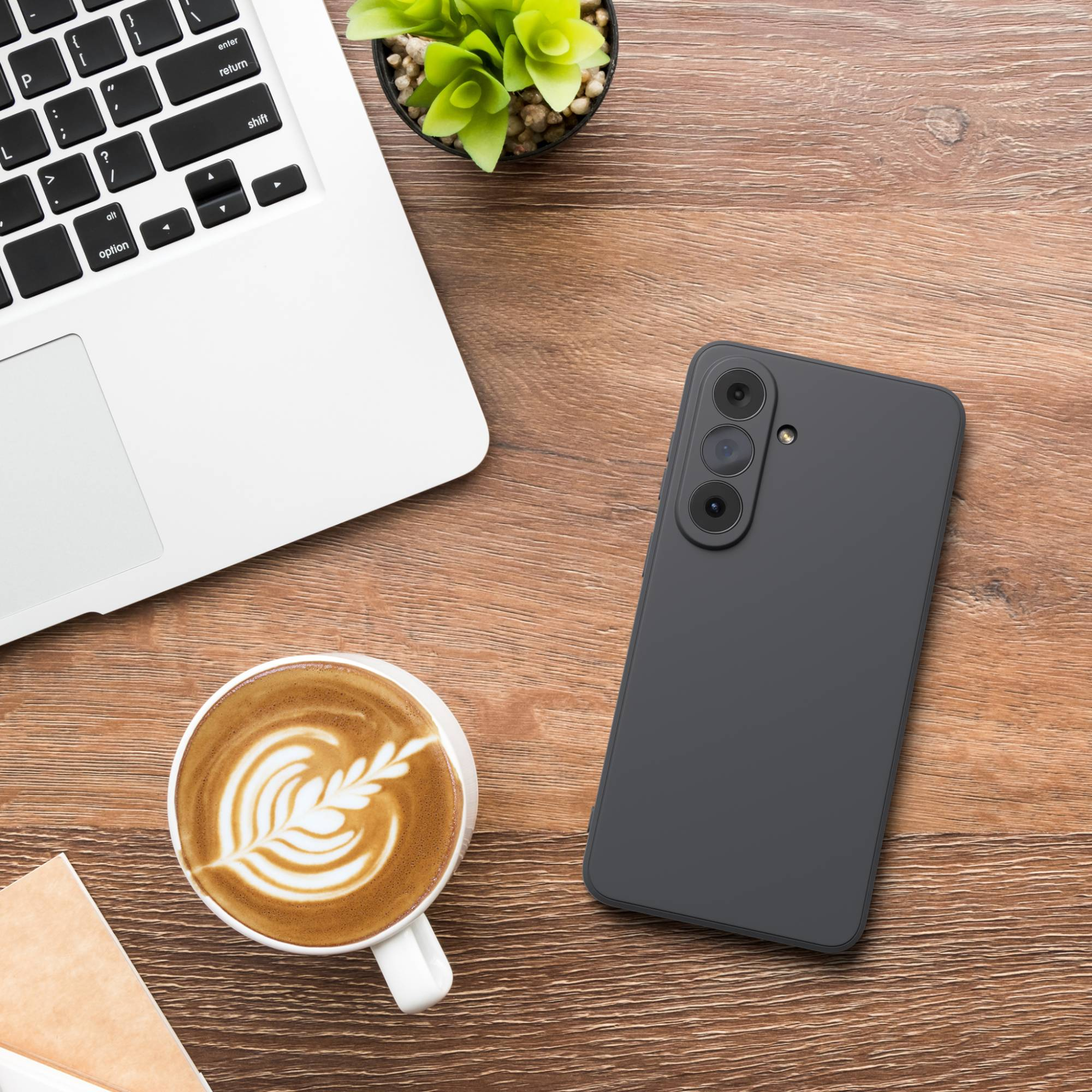 Ein Laptop, ein Smartphone, eine Kaffeetasse und eine Pflanze auf einem Holztisch.