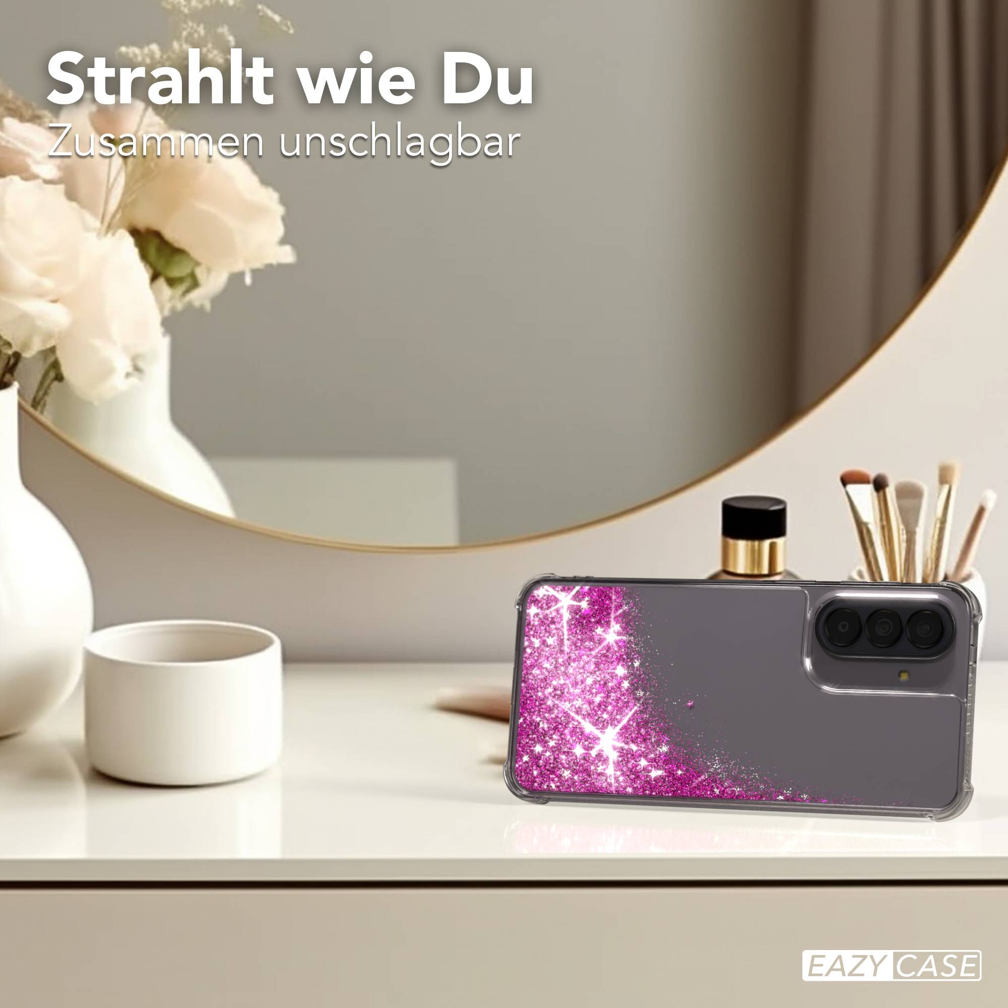 Graues Handy mit glitzerndem Pink auf dem Tisch, Spiegel und Blumen im Hintergrund.