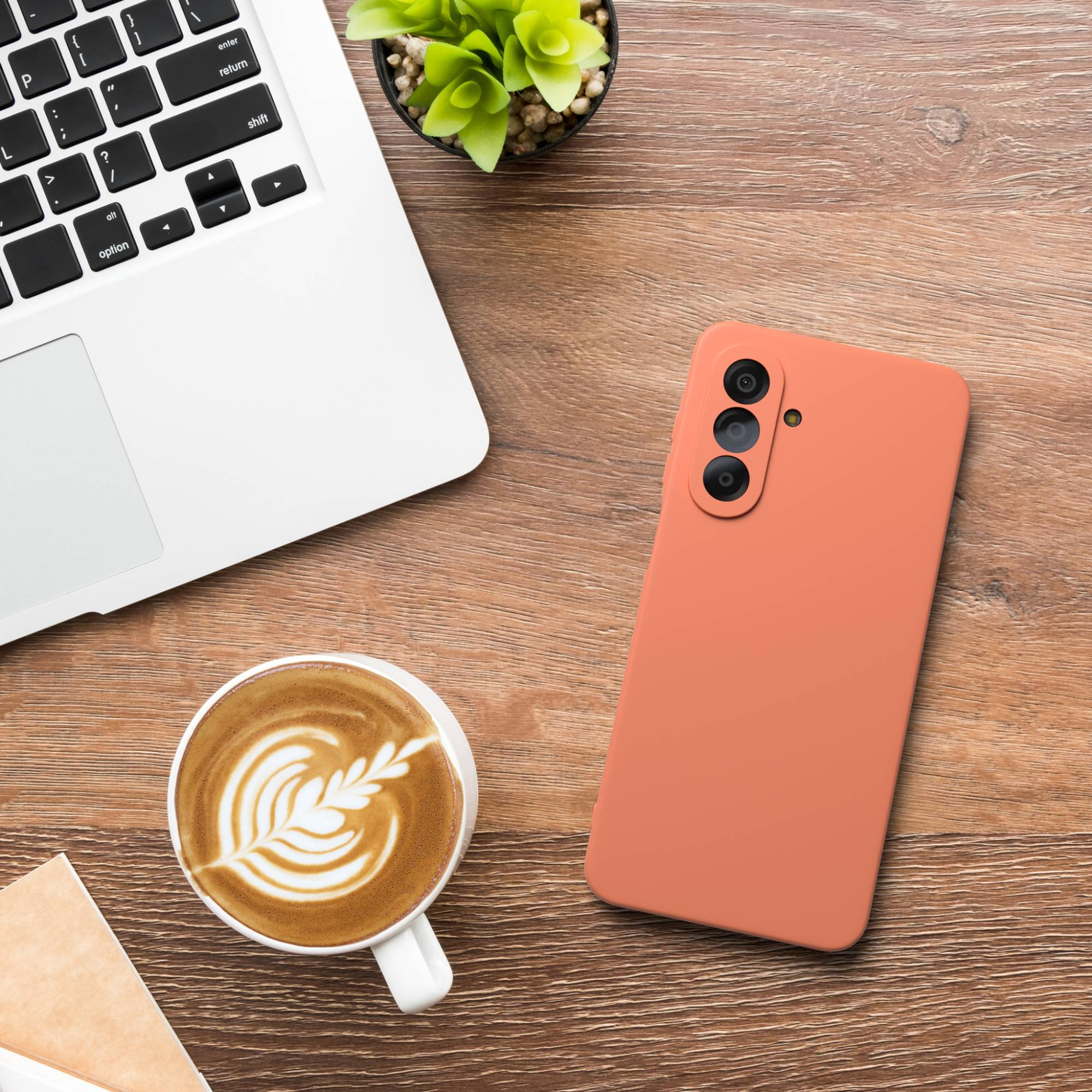 Ein Laptop, eine Kaffeetasse mit Latte Art und ein Handy liegen auf einem Holztisch.