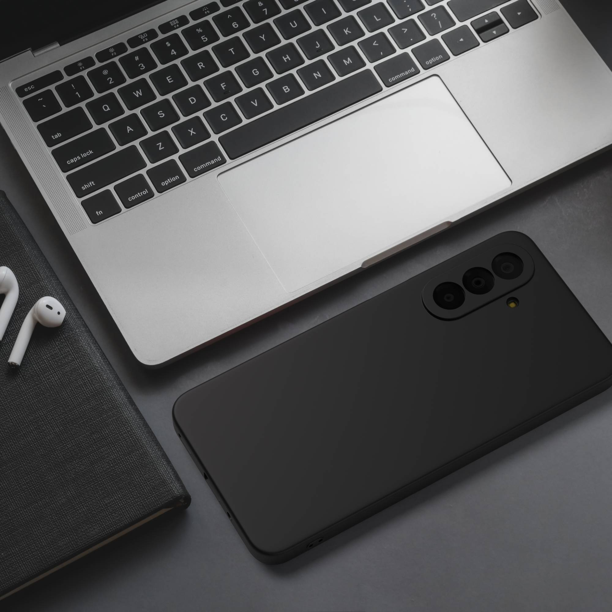 Ein schwarzes Smartphone liegt neben einem geöffneten Laptop, Kopfhörern und einem Notizbuch.