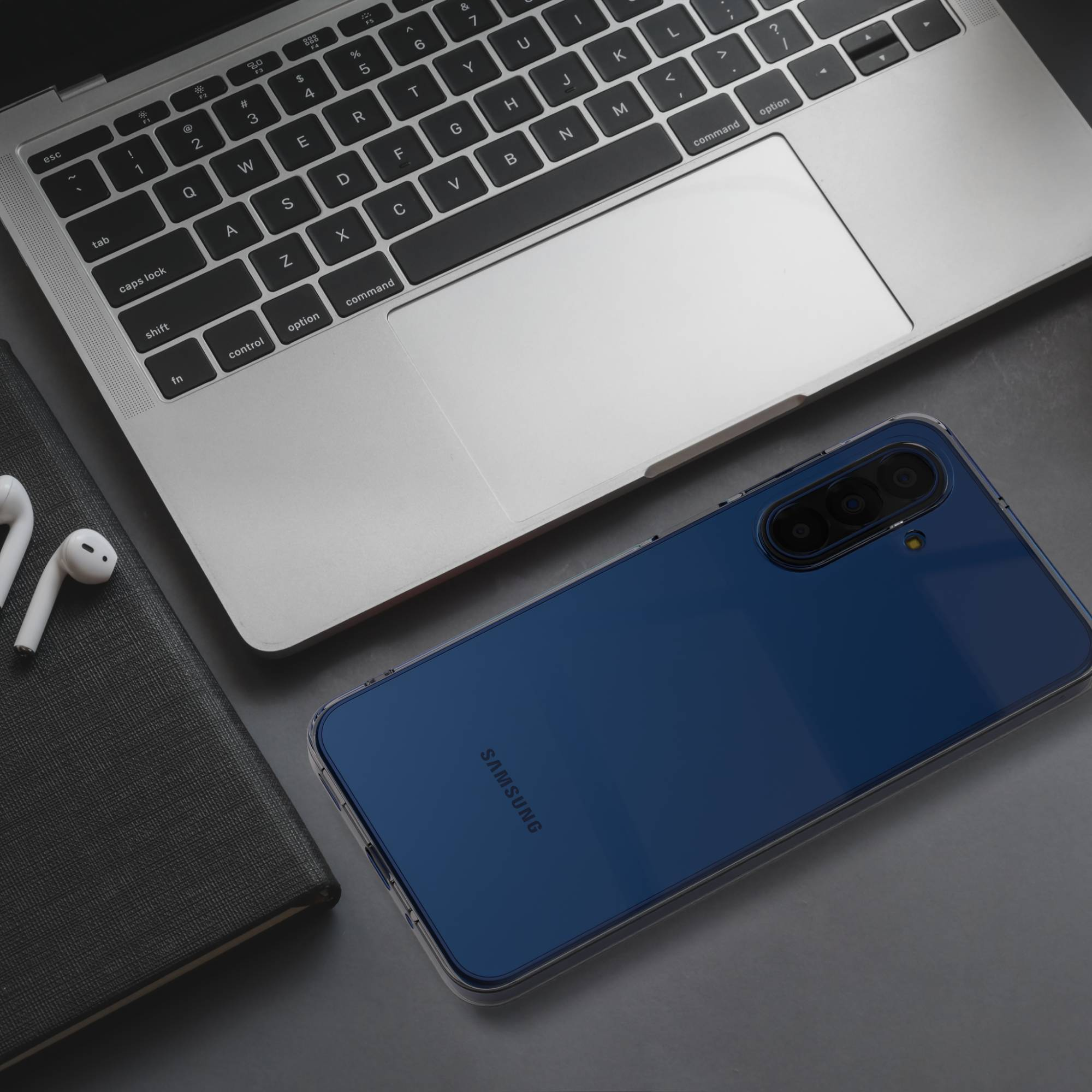 Ein blauer Samsung Handy liegt neben einem Laptop, Kopfhörern und einem Notizbuch.