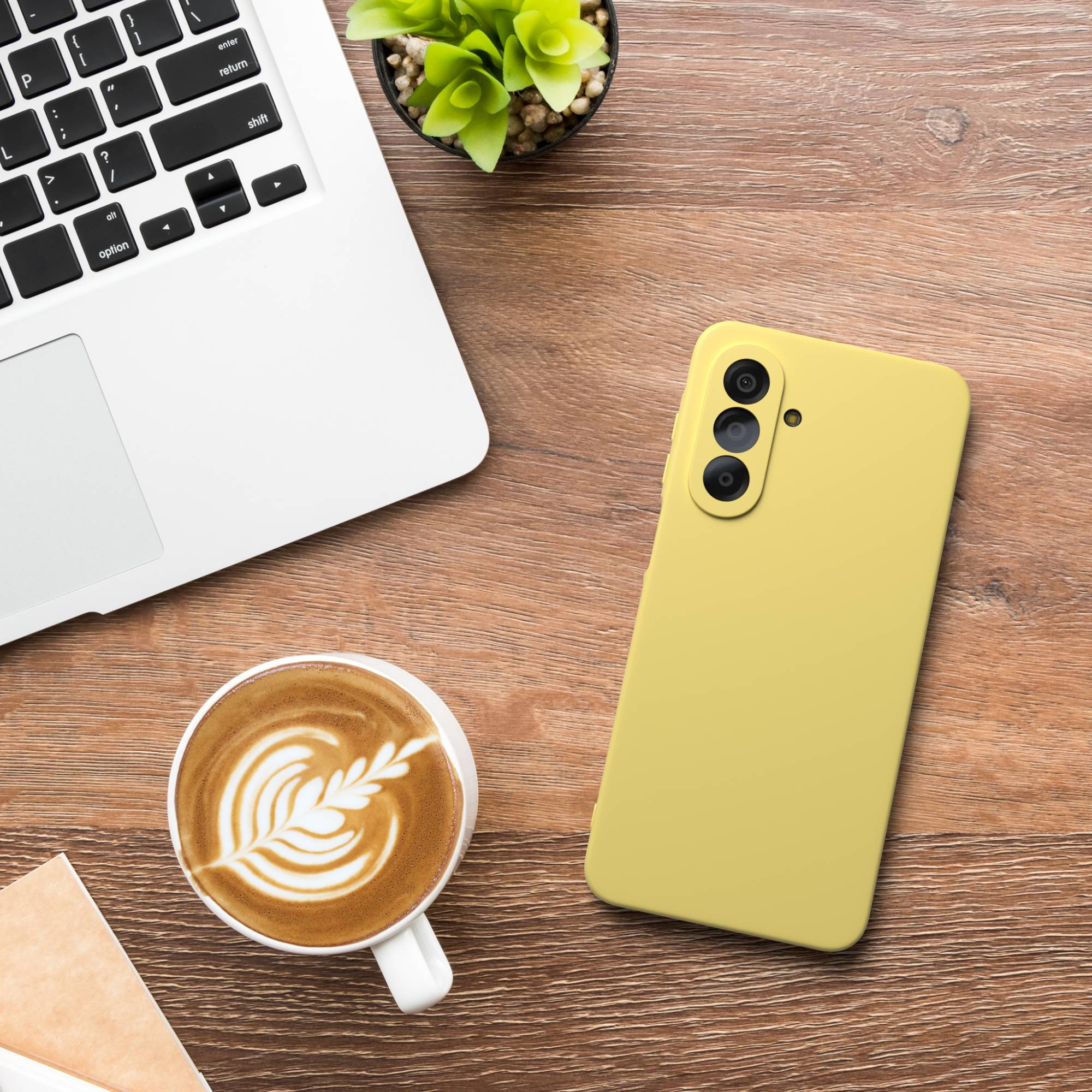 Ein Laptop, gelbes Handy, Kaffee mit Latte Art und Pflanze auf einem Holzschreibtisch.