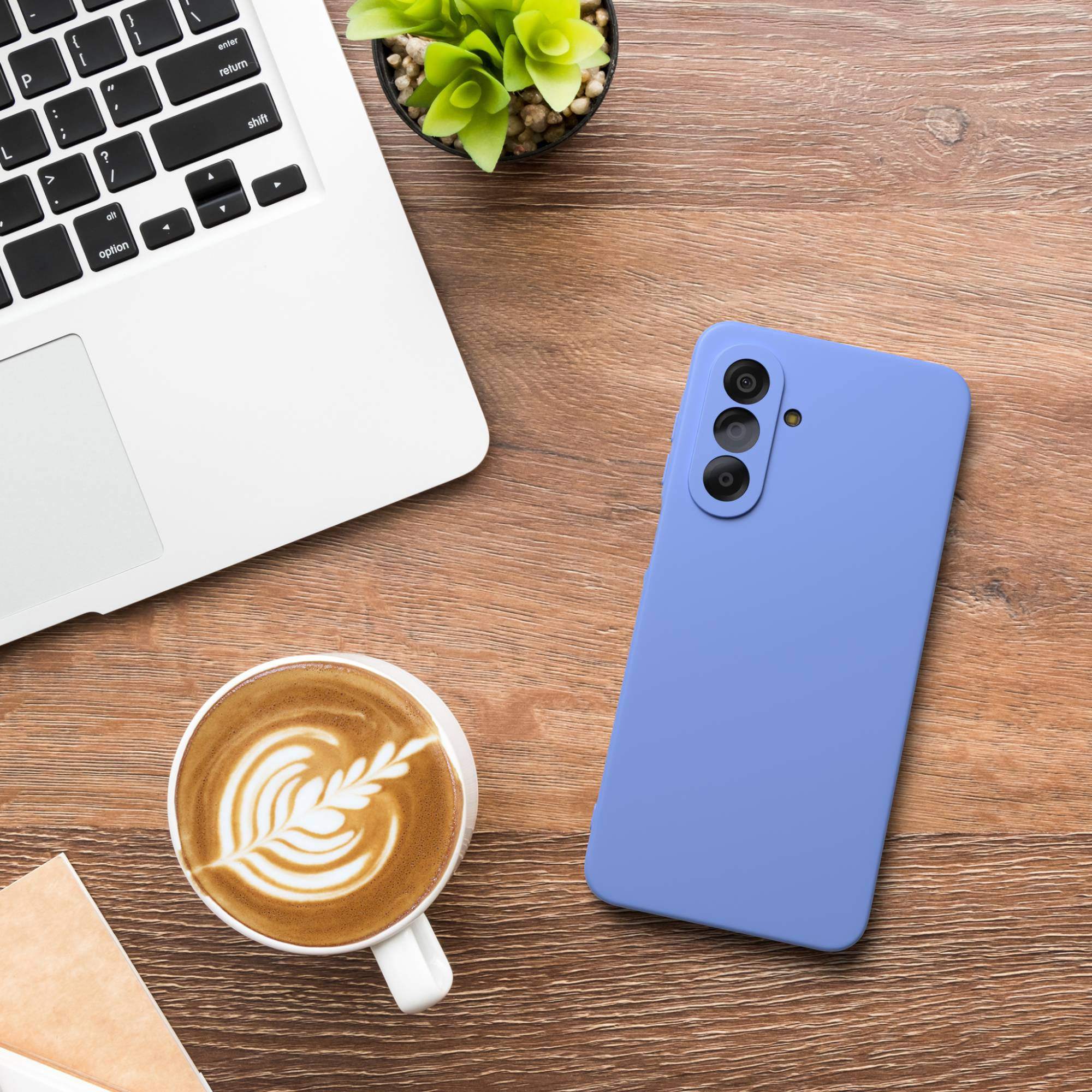 Ein Laptop, eine Kaffeetasse mit Latte Art, ein Smartphone und eine Pflanze auf einem Holztisch.