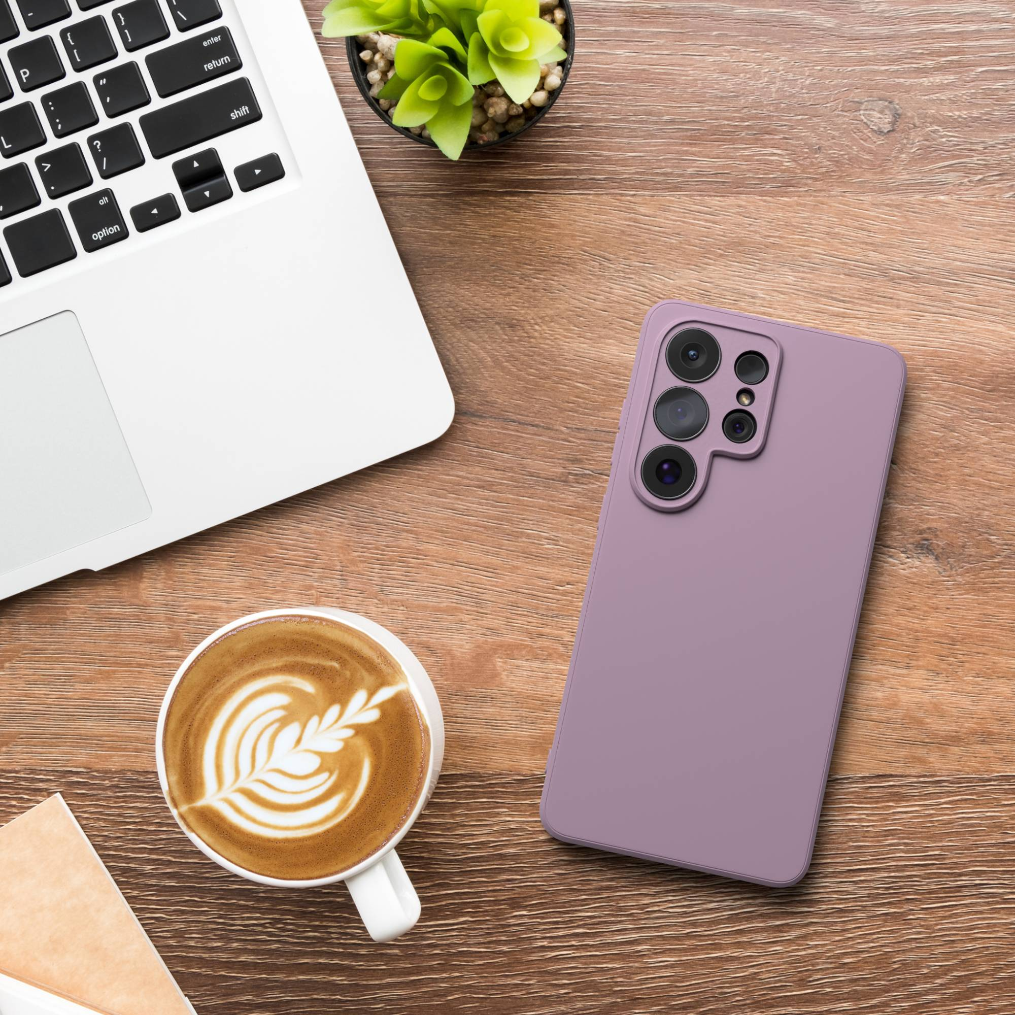 Ein Laptop, eine Kaffeetasse mit Latte Art und ein Handy liegen auf einem Holztisch.