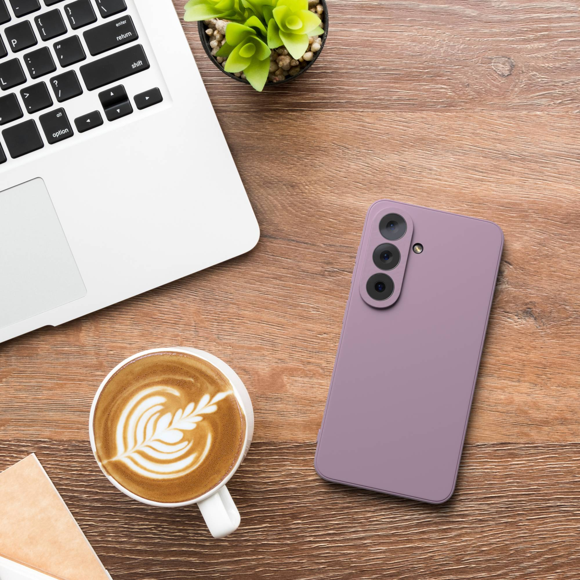 Ein Laptop, ein Handy, Kaffee und eine Pflanze auf einem Holztisch.
