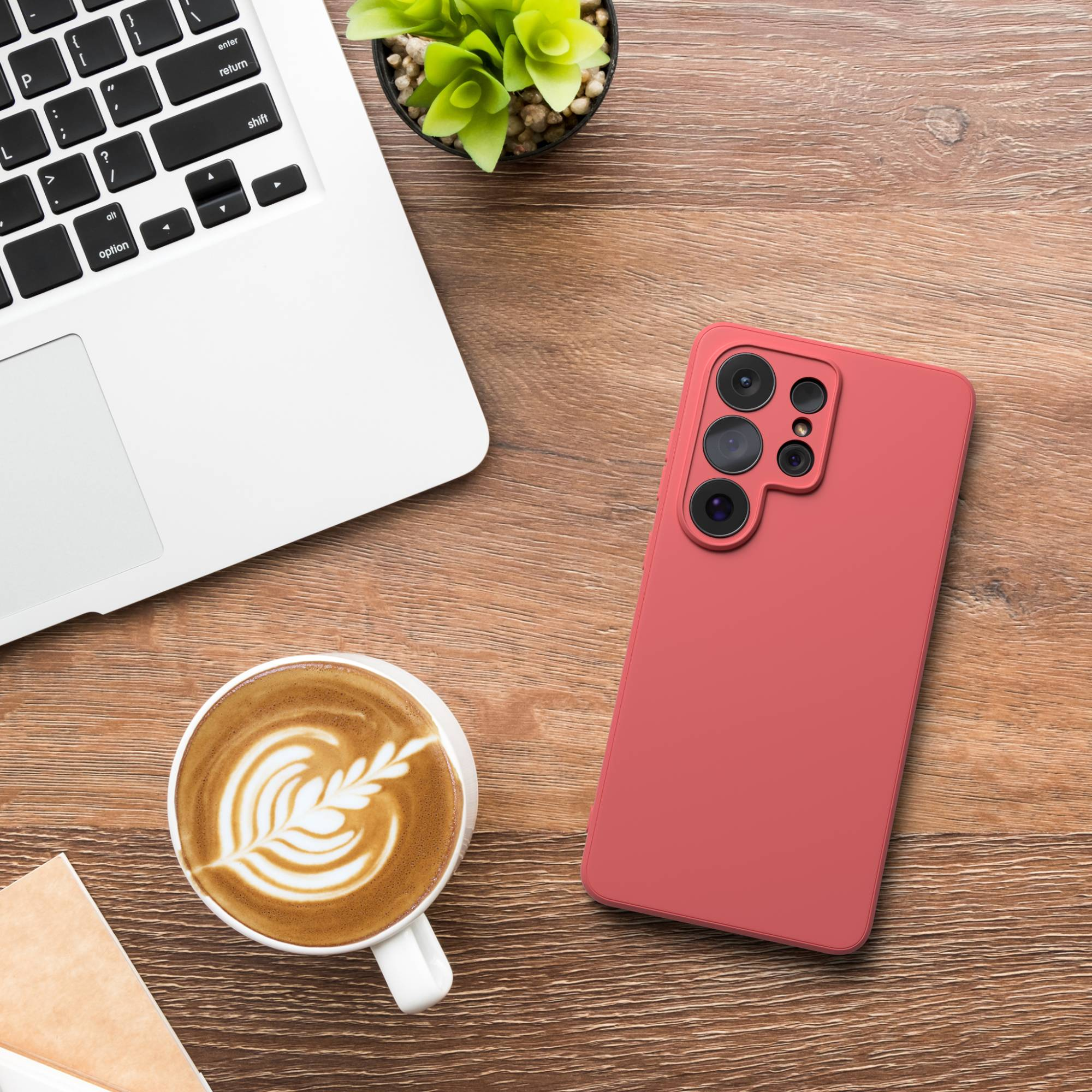 Ein Laptop, ein Handy-Case, Kaffee und eine Pflanze auf Holztisch.