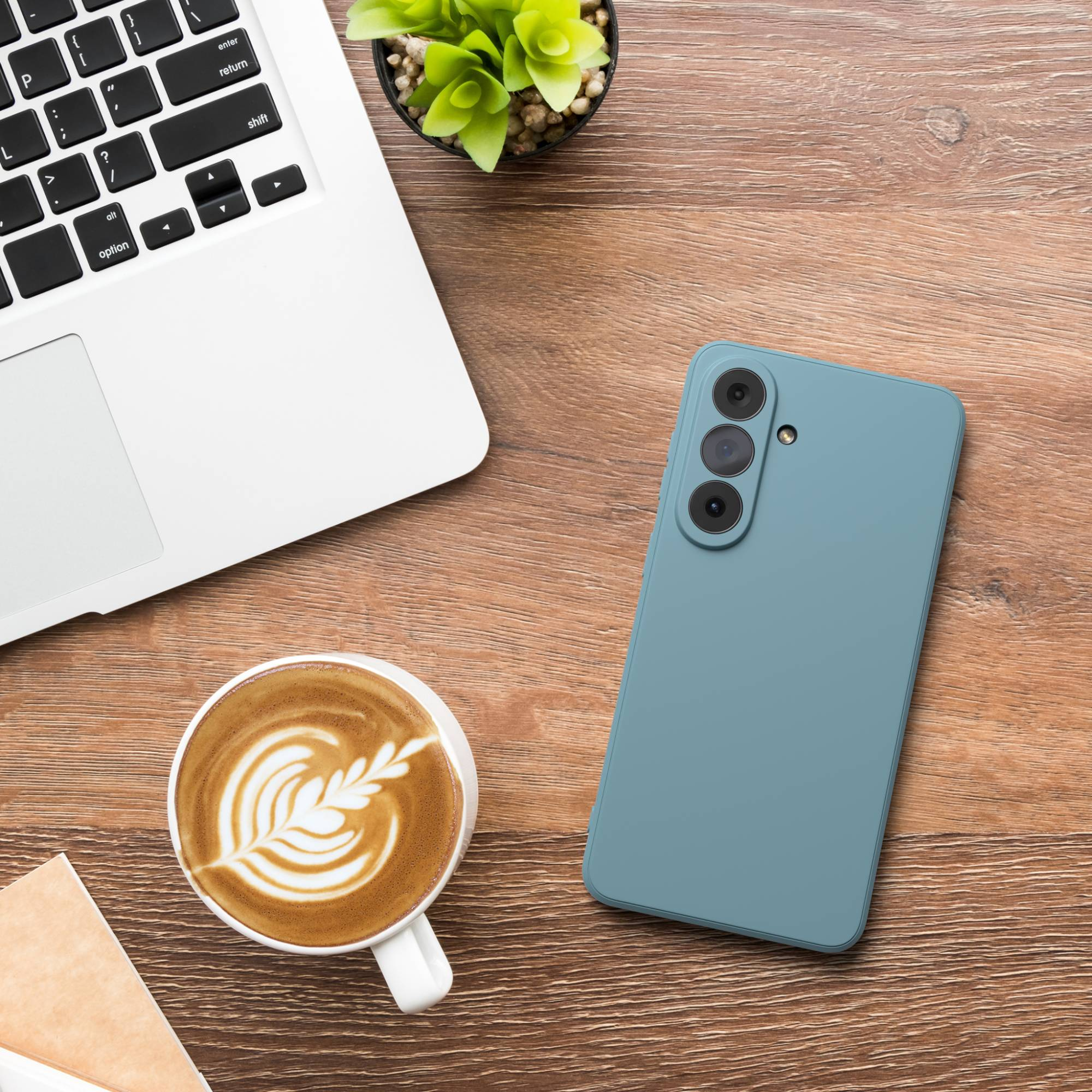 Ein Laptop, ein türkisfarbenes Smartphone, eine Kaffeetasse und eine Pflanze auf einem Holztisch.