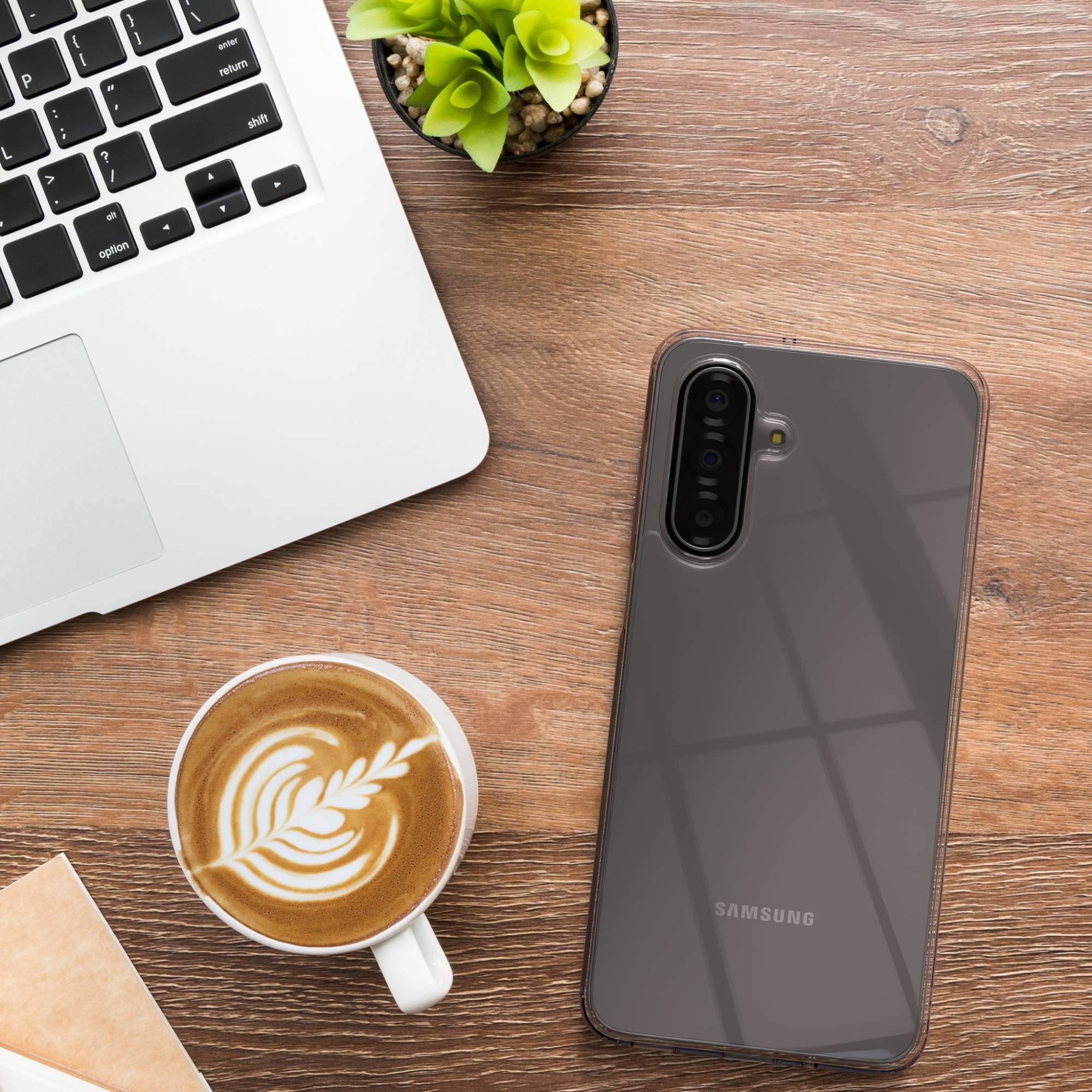 Ein Laptop, eine Kaffeetasse mit Latte Art und ein Smartphone auf einem Holztisch.