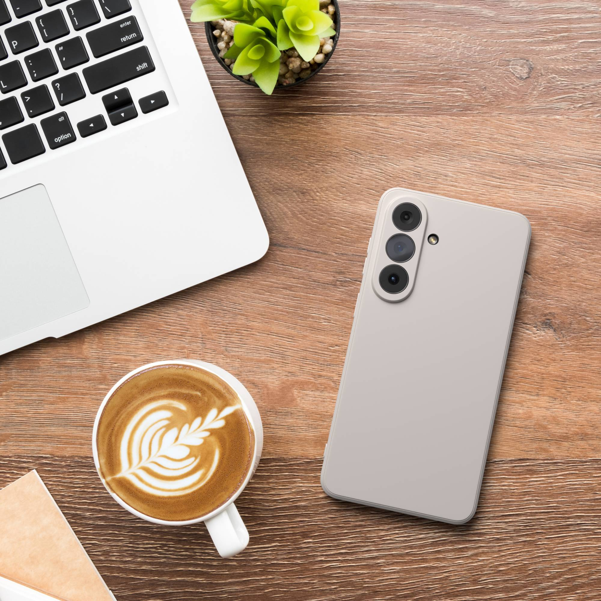 Ein Laptop, ein Handy und eine Kaffeetasse mit Latte Art auf einem Holztisch.