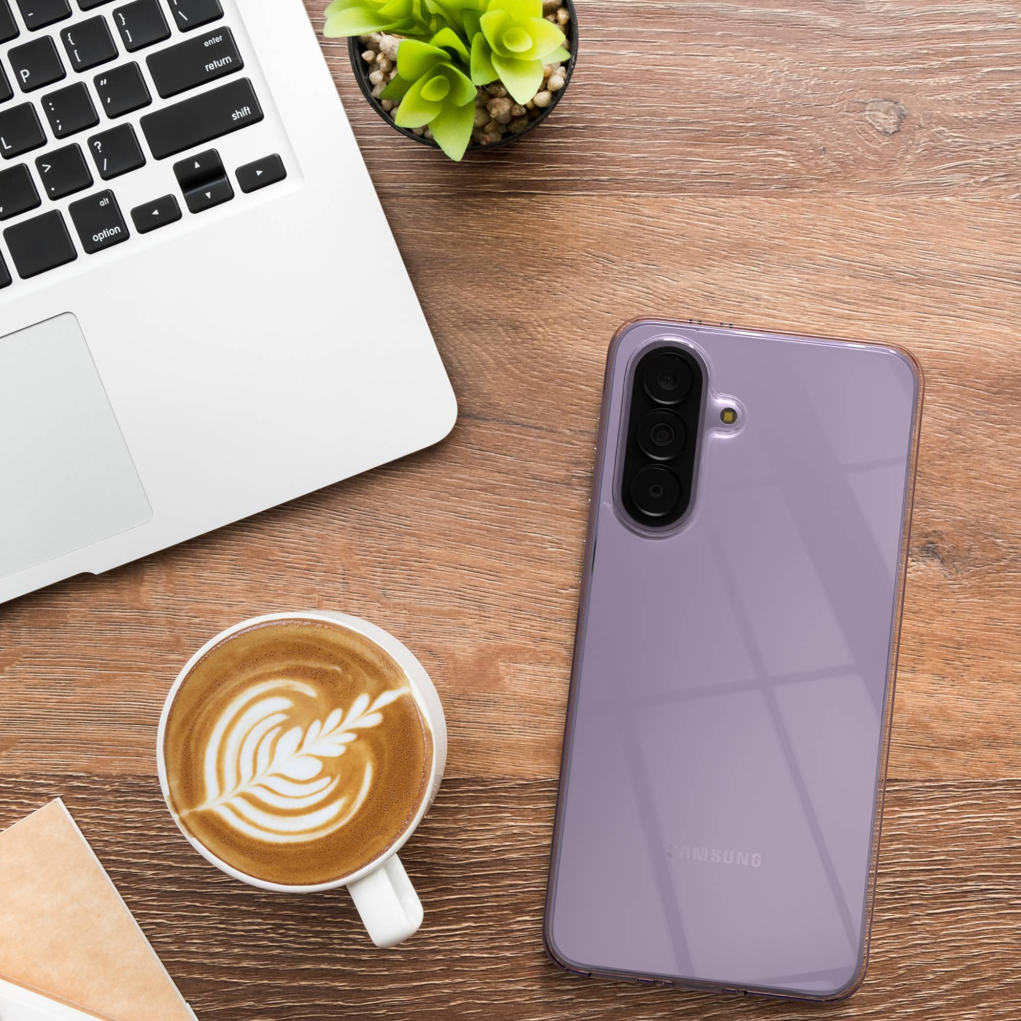 Ein Laptop, eine Kaffeetasse mit Latte Art und ein lilafarbenes Smartphone liegen auf einem Holztisch.