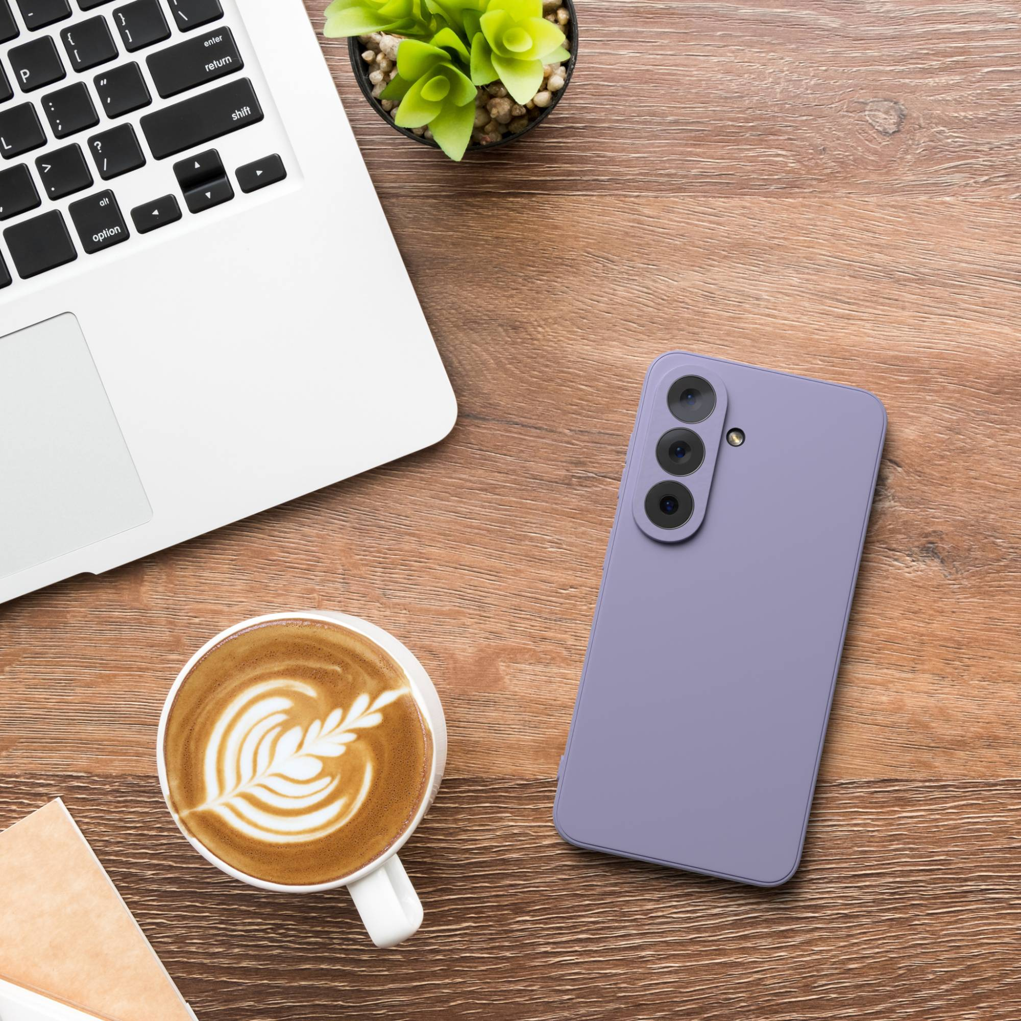 Ein Laptop, eine Kaffeetasse mit Latte Art, ein Handy und eine Pflanze auf einem Holztisch.