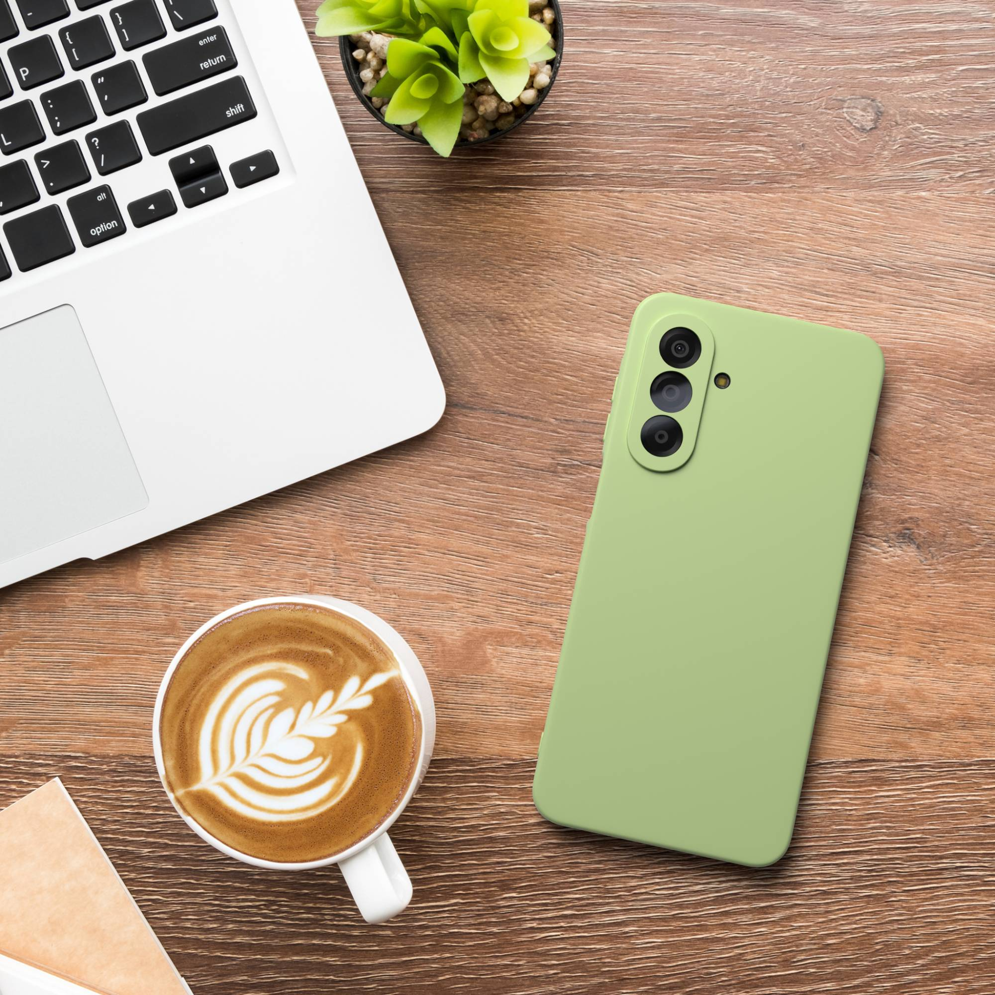 Ein Laptop, eine grüne Handyhülle, Kaffee und eine Pflanze auf Holztisch.