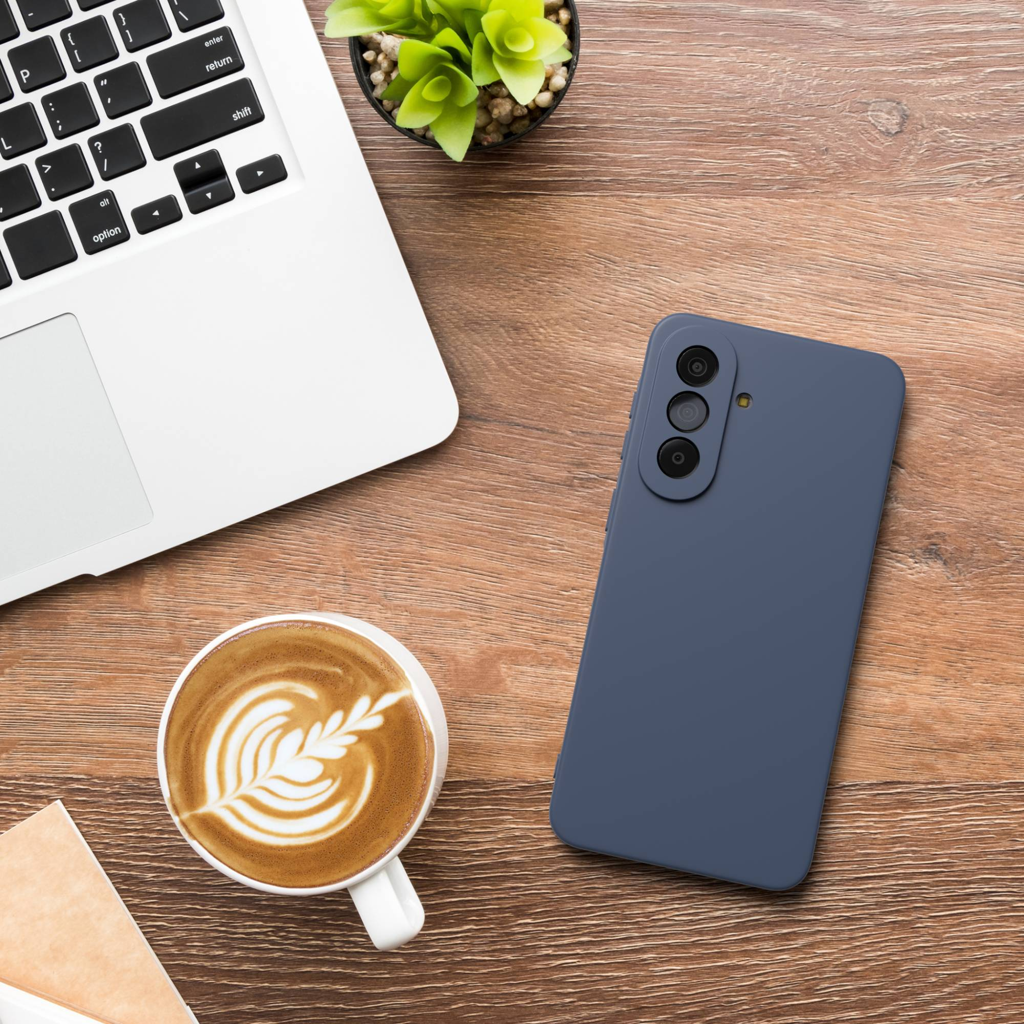 Ein Laptop, ein Handy, eine Kaffeetasse und eine Pflanze auf einem Holztisch.