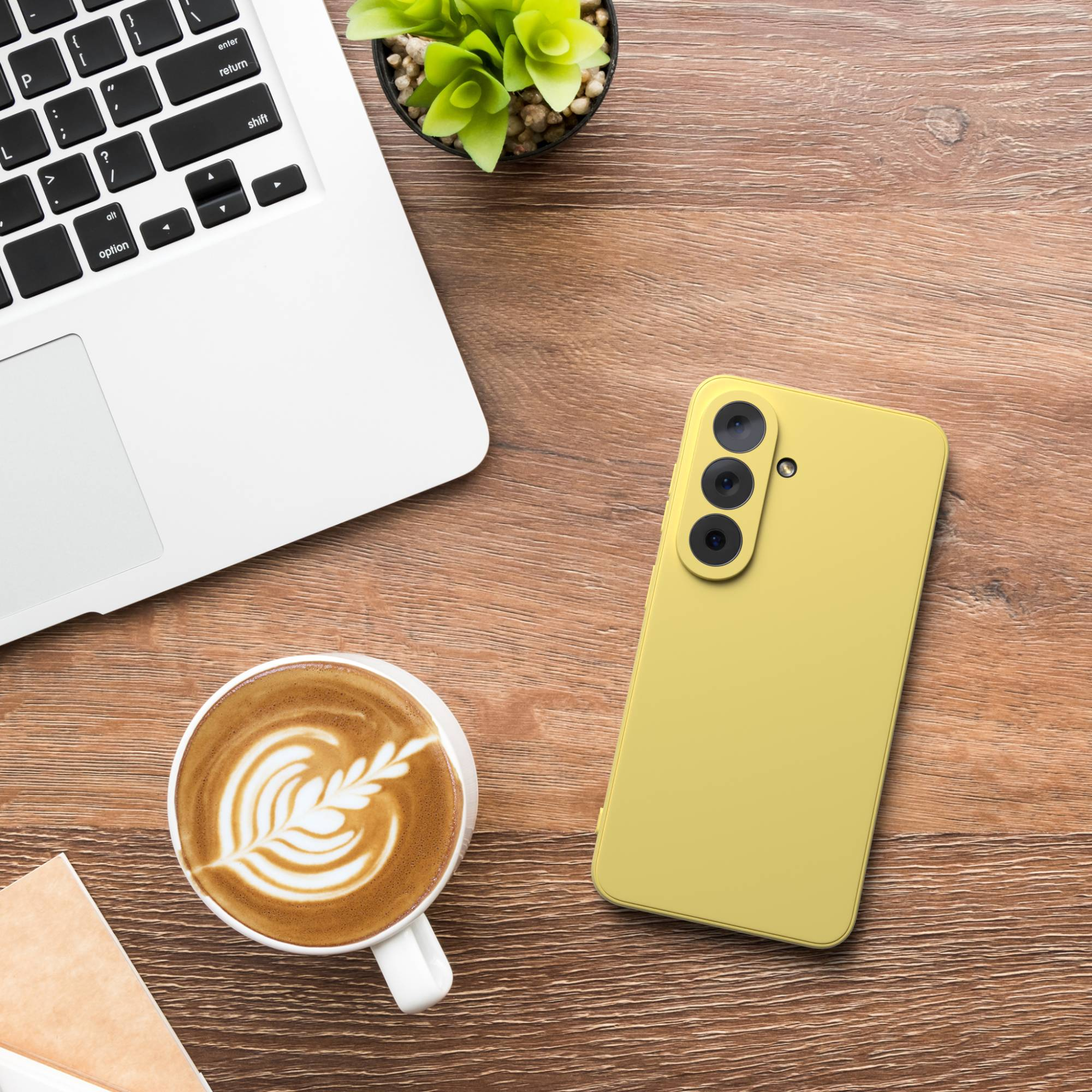 Ein gelbes Smartphone, eine Kaffeetasse und ein Laptop auf einem Holztisch.