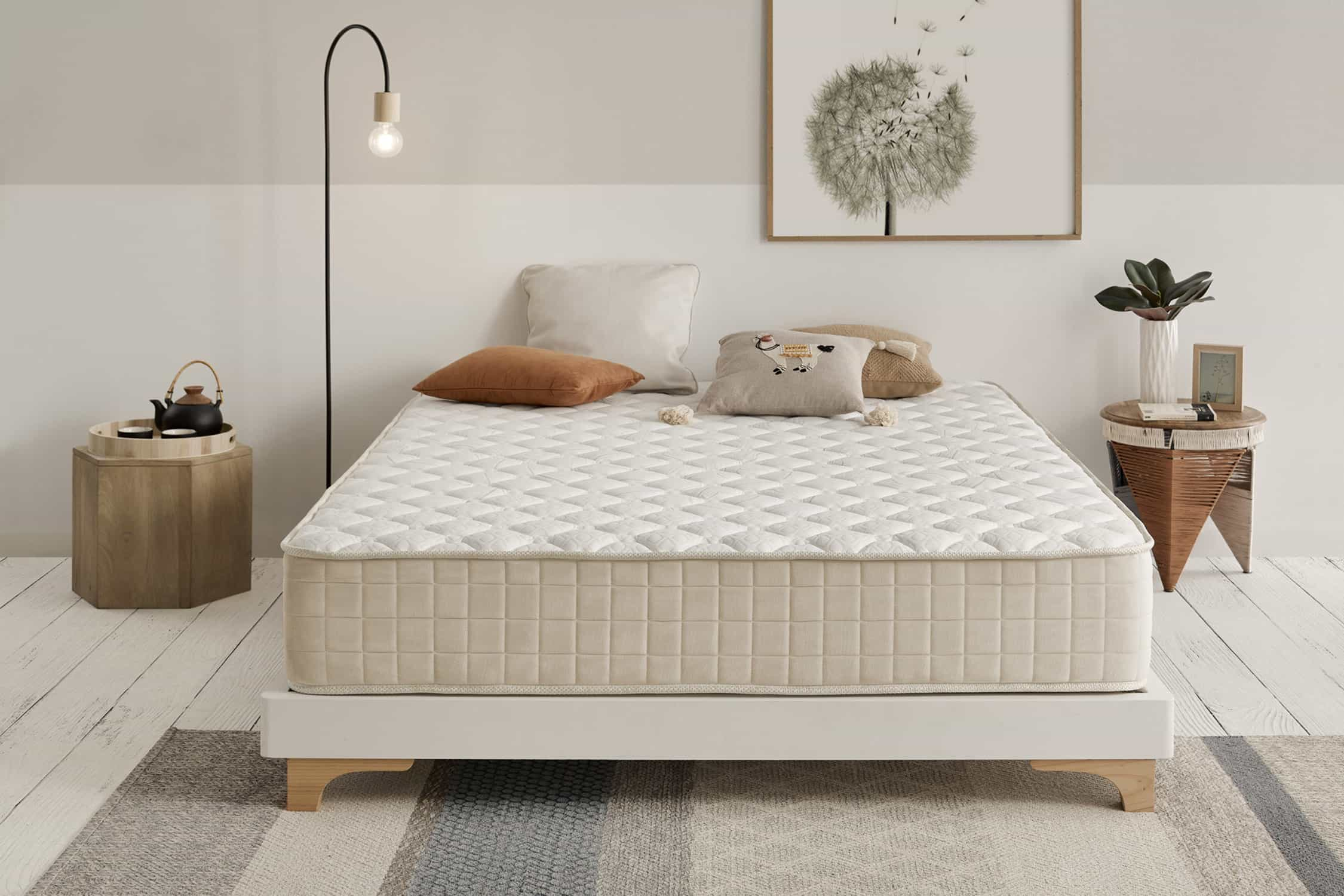 Una cama blanca con colchón, cojines, lámpara y cuadro en la pared.