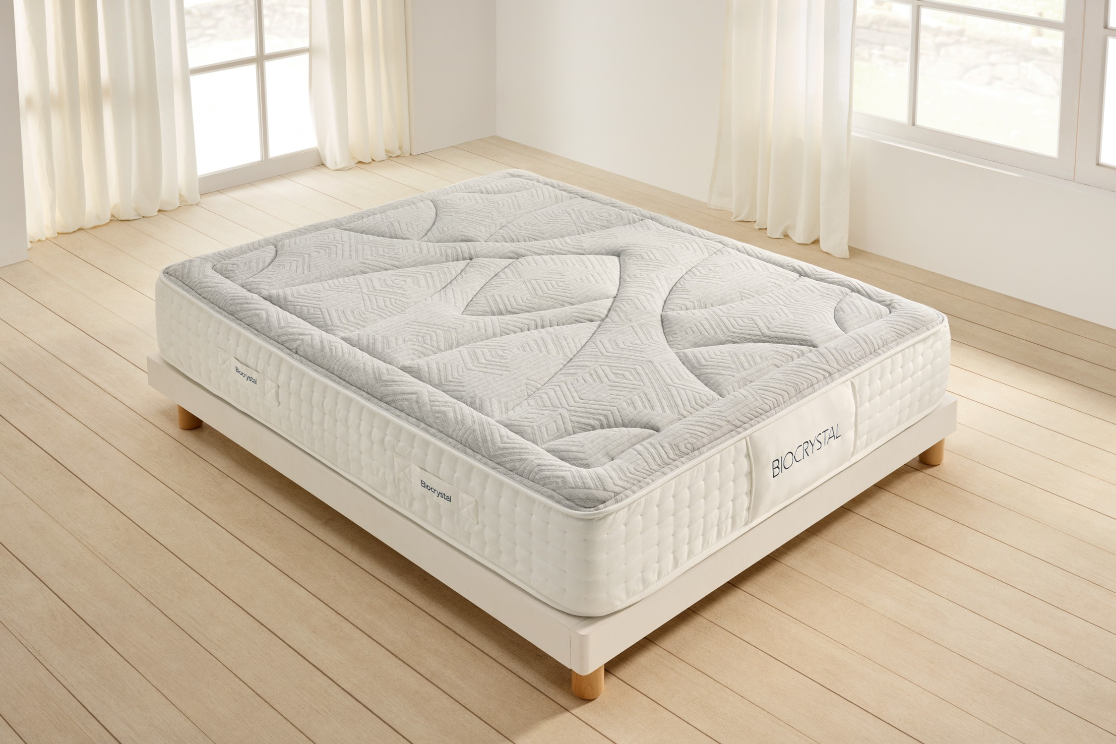 Una cama blanca con colchón acolchado sobre suelo de madera.