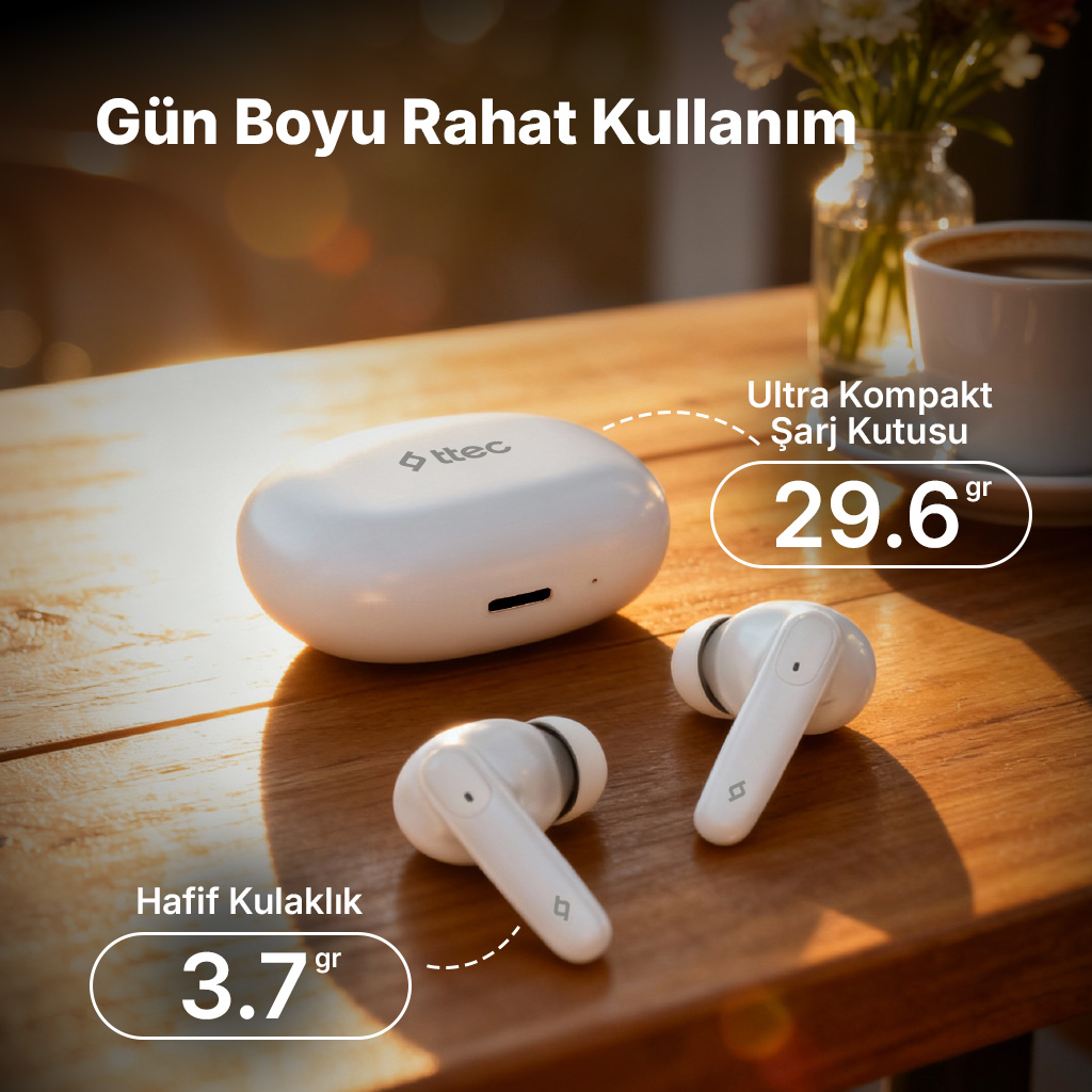 Ahşap masada beyaz Ttec kulaklıklar ve şarj kutusu. Kahve ve çiçekler arka planda.