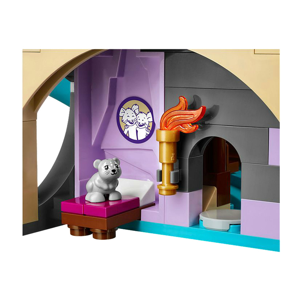 Un gattino Lego grigio siede su una base viola e marrone davanti a un muro viola con un emblema.