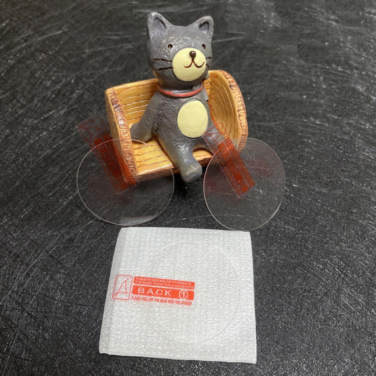 Scultura di gatto grigio su sedia a rotelle con ruote trasparenti e adesivo.
