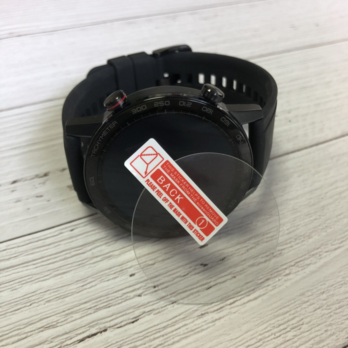 Smartwatch nera con adesivo protettivo sullo schermo, su superficie di legno.