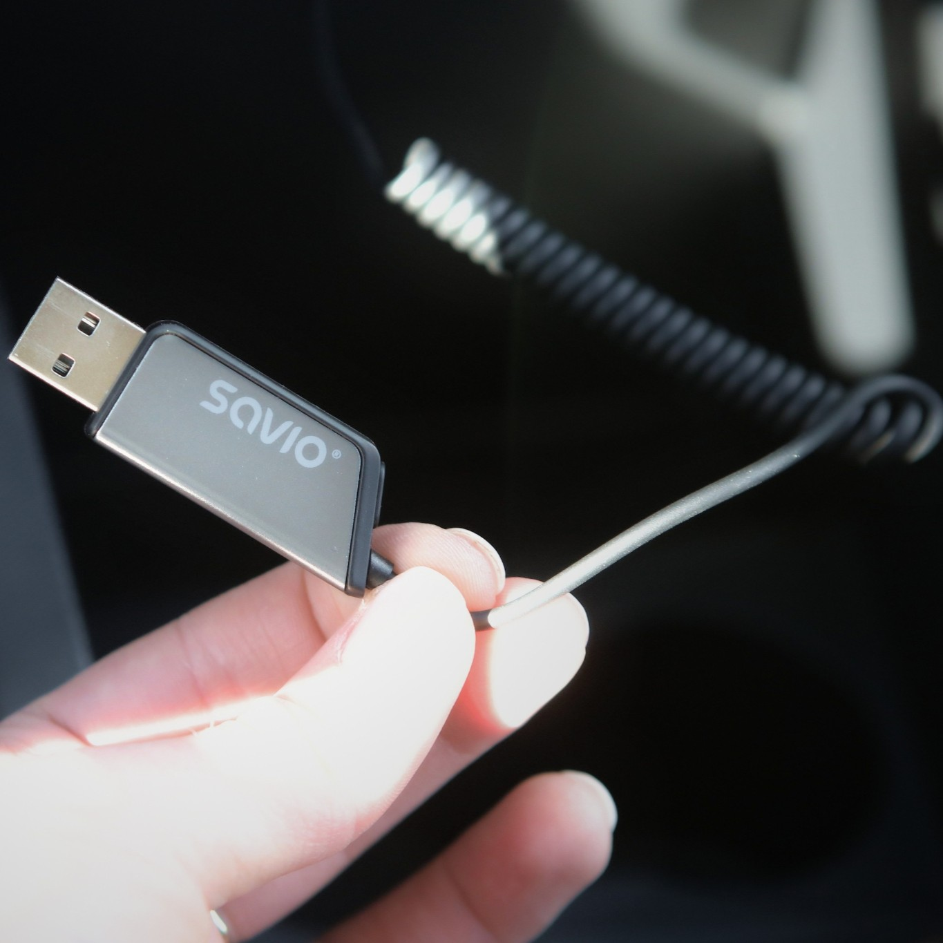 Dłoń trzymająca szary pendrive z logo 'SAVIO' i sprężystym kablem.