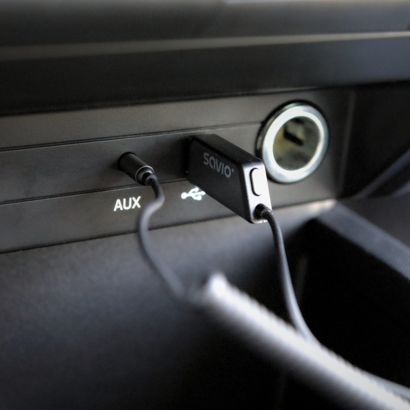 Czarne urządzenie Savio podłączone do portu USB i wejścia AUX w samochodzie.