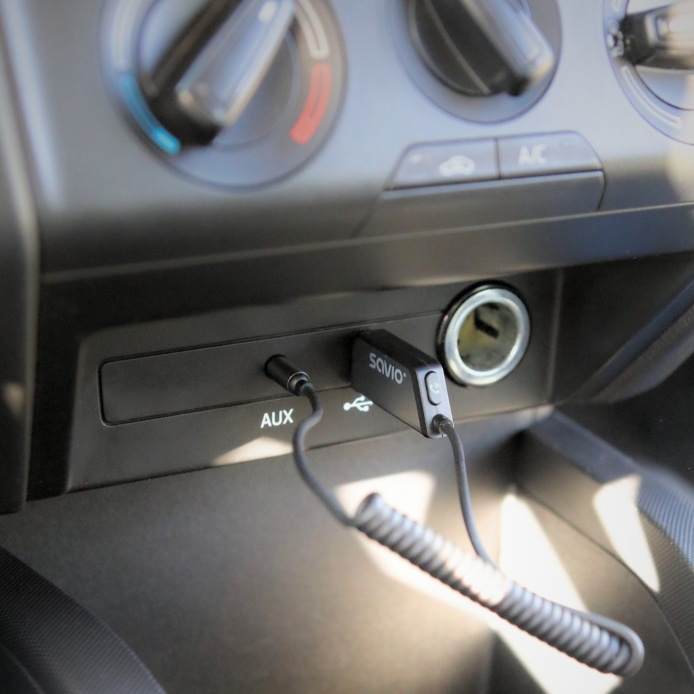 Wnętrze samochodu: Adapter AUX i USB podłączony do deski rozdzielczej. Widoczne regulatory klimatu.