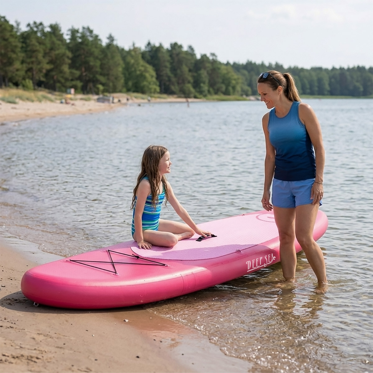 Frau und Mädchen auf pinkem Paddleboard am Sandstrand mit Bäumen im Hintergrund.