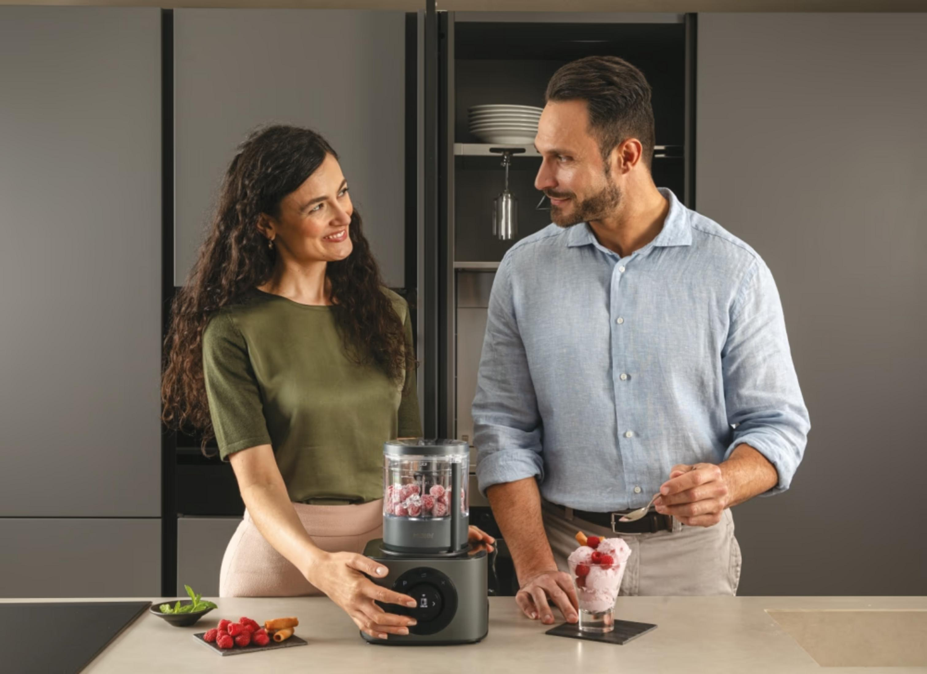 Una coppia in cucina prepara il gelato. Una donna aziona un frullatore, un uomo guarnisce un bicchiere di gelato.