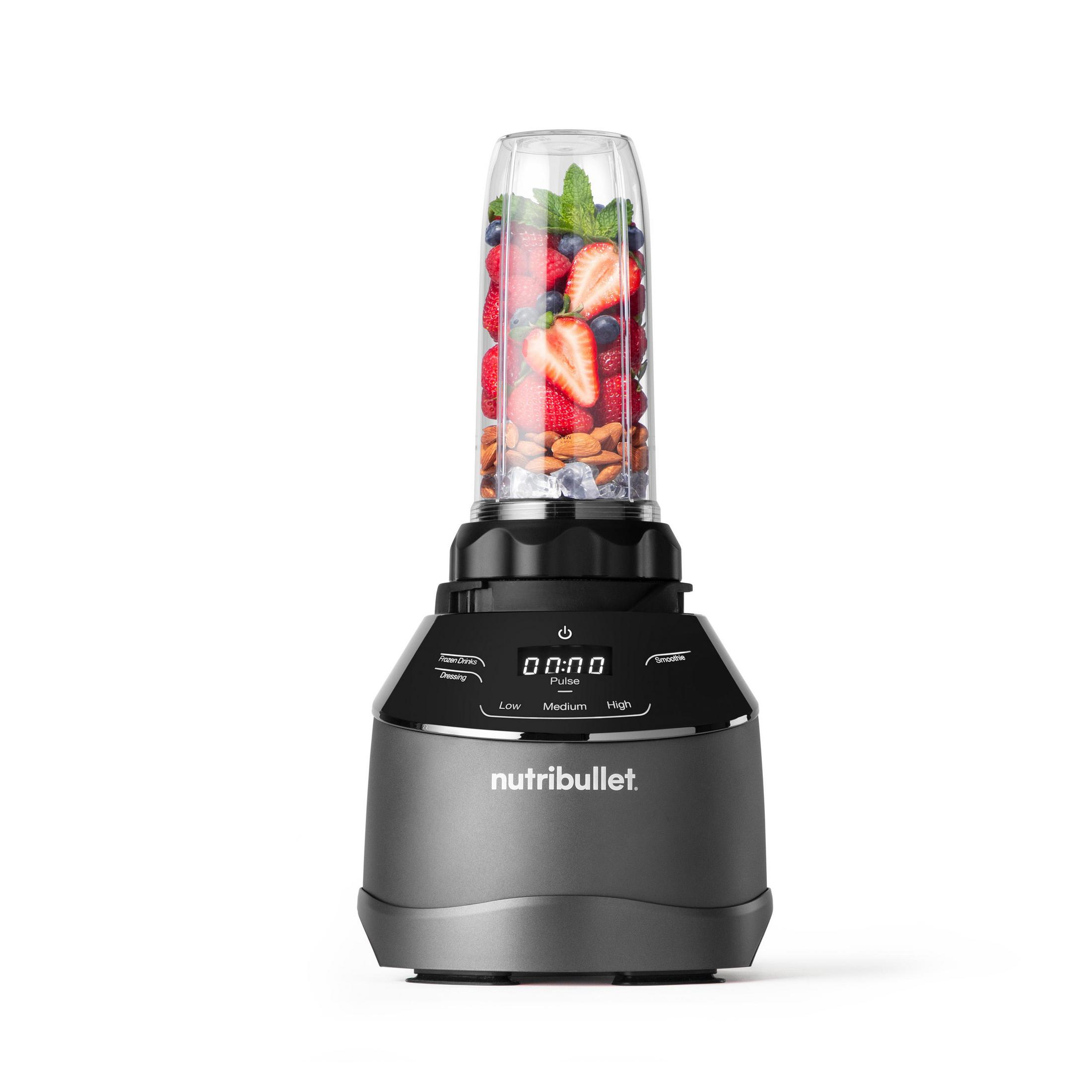 Un frullatore NutriBullet grigio con frutta e noci nel contenitore.