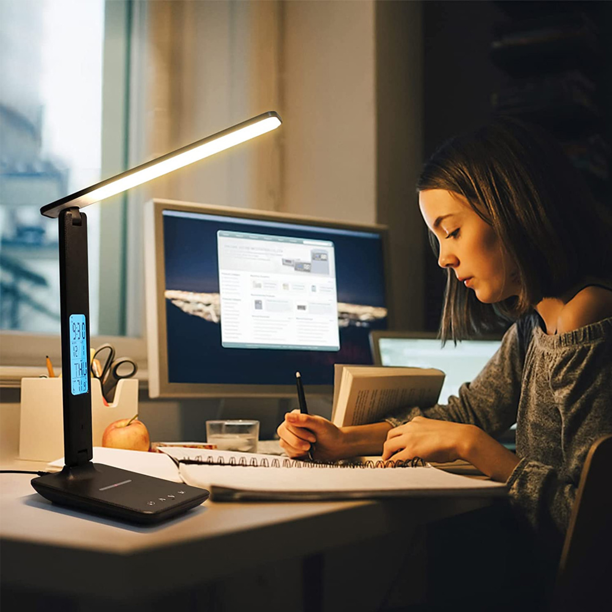 Eine junge Frau lernt am Schreibtisch, beleuchtet von einer Lampe mit Digitalanzeige.