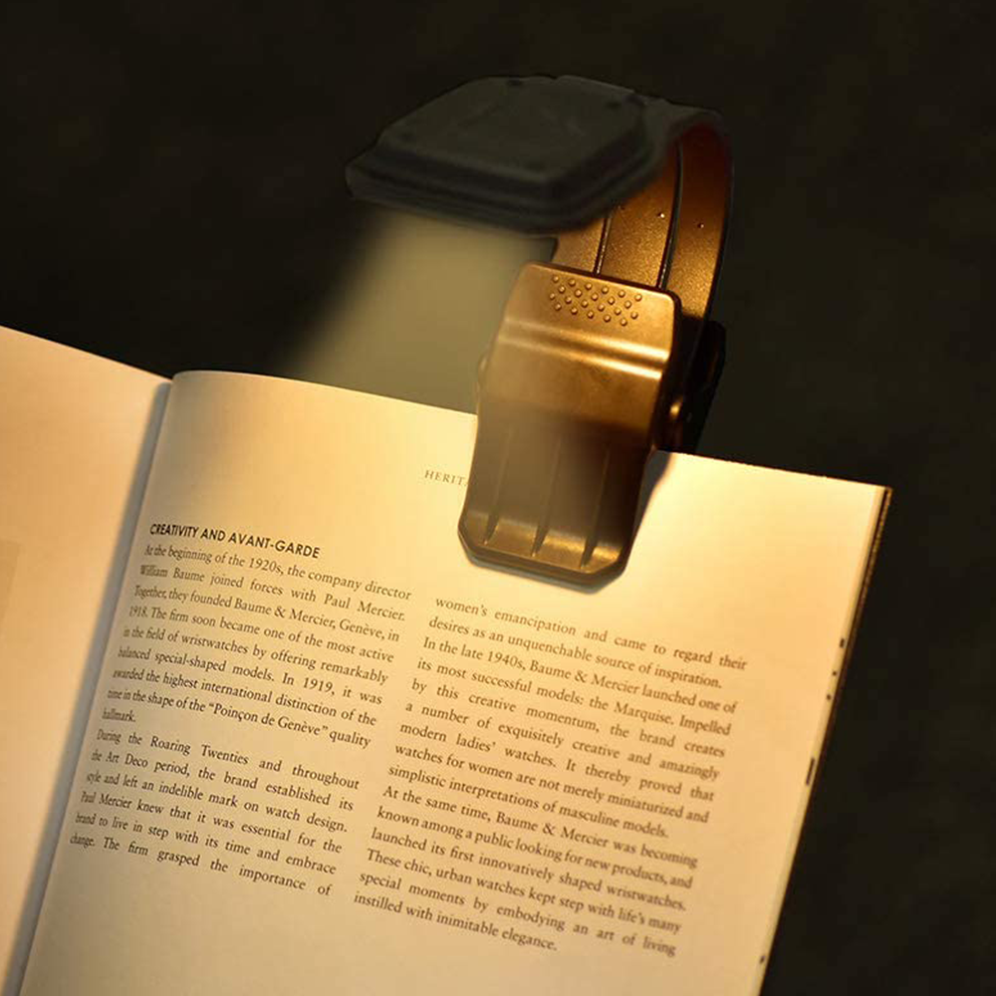 Eine schwarze Buchleuchte klemmt auf einem offenen Buch und beleuchtet den Text warm.