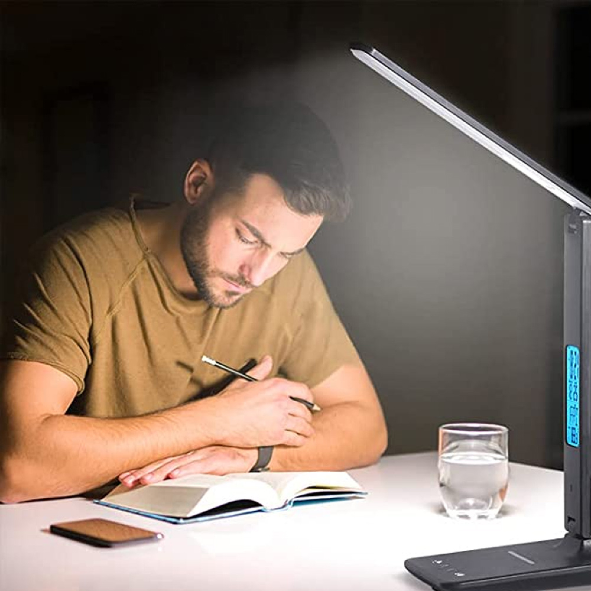 Mann schreibt in ein Buch, beleuchtet von Schreibtischlampe mit Uhr.