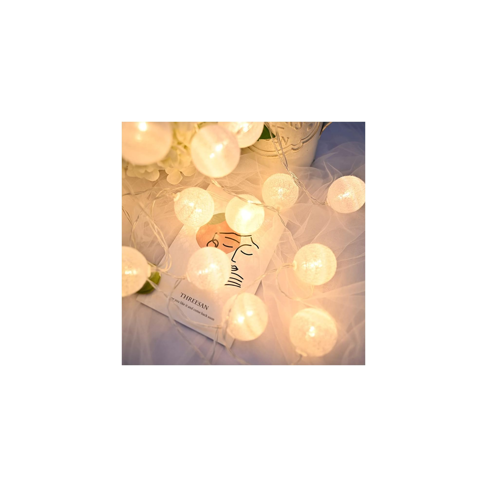 Lichterkette mit weißen Kugeln leuchtet über einer Kunstkarte mit Gesicht.