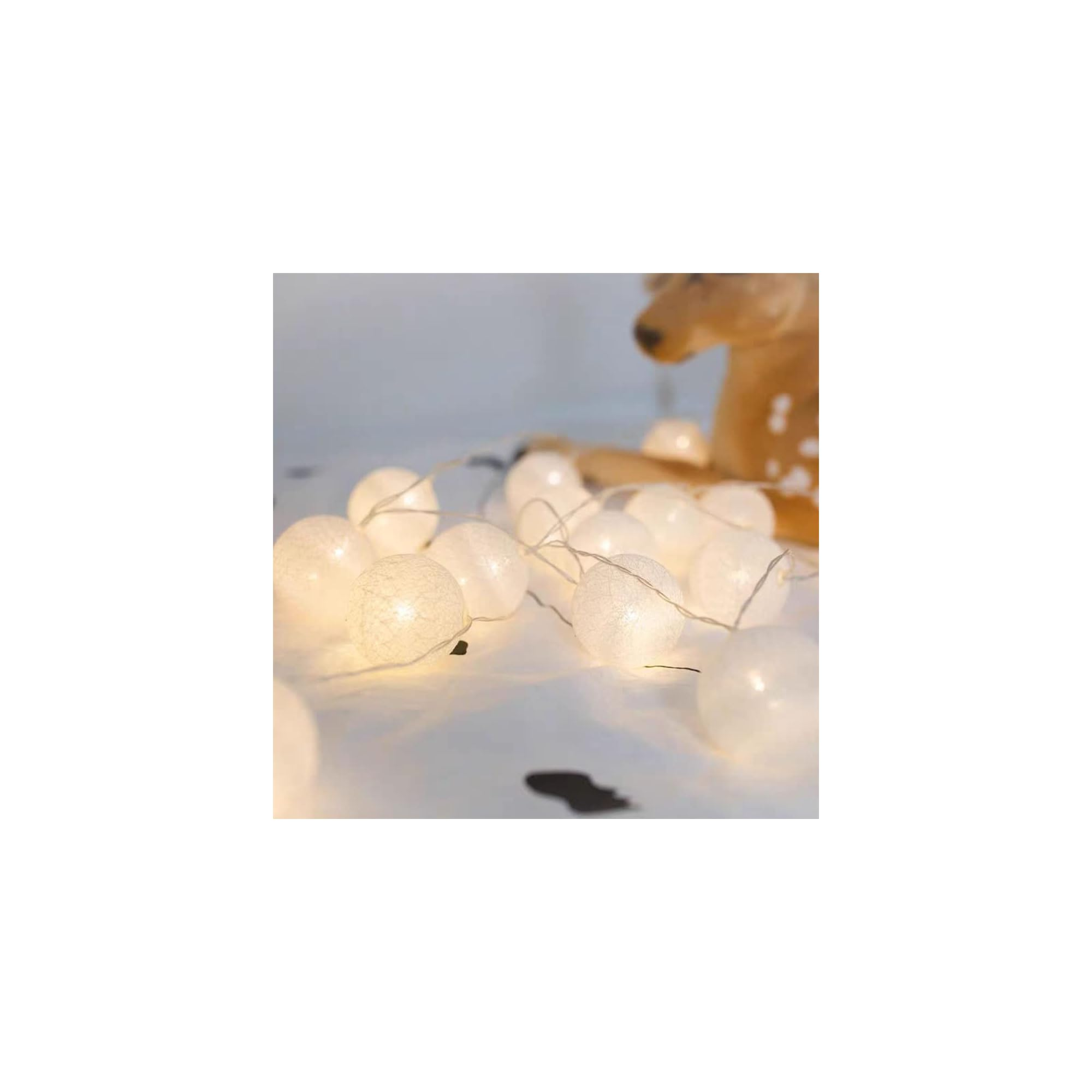 Eine Lichterkette mit weißen Kugeln und einem Reh im Hintergrund.