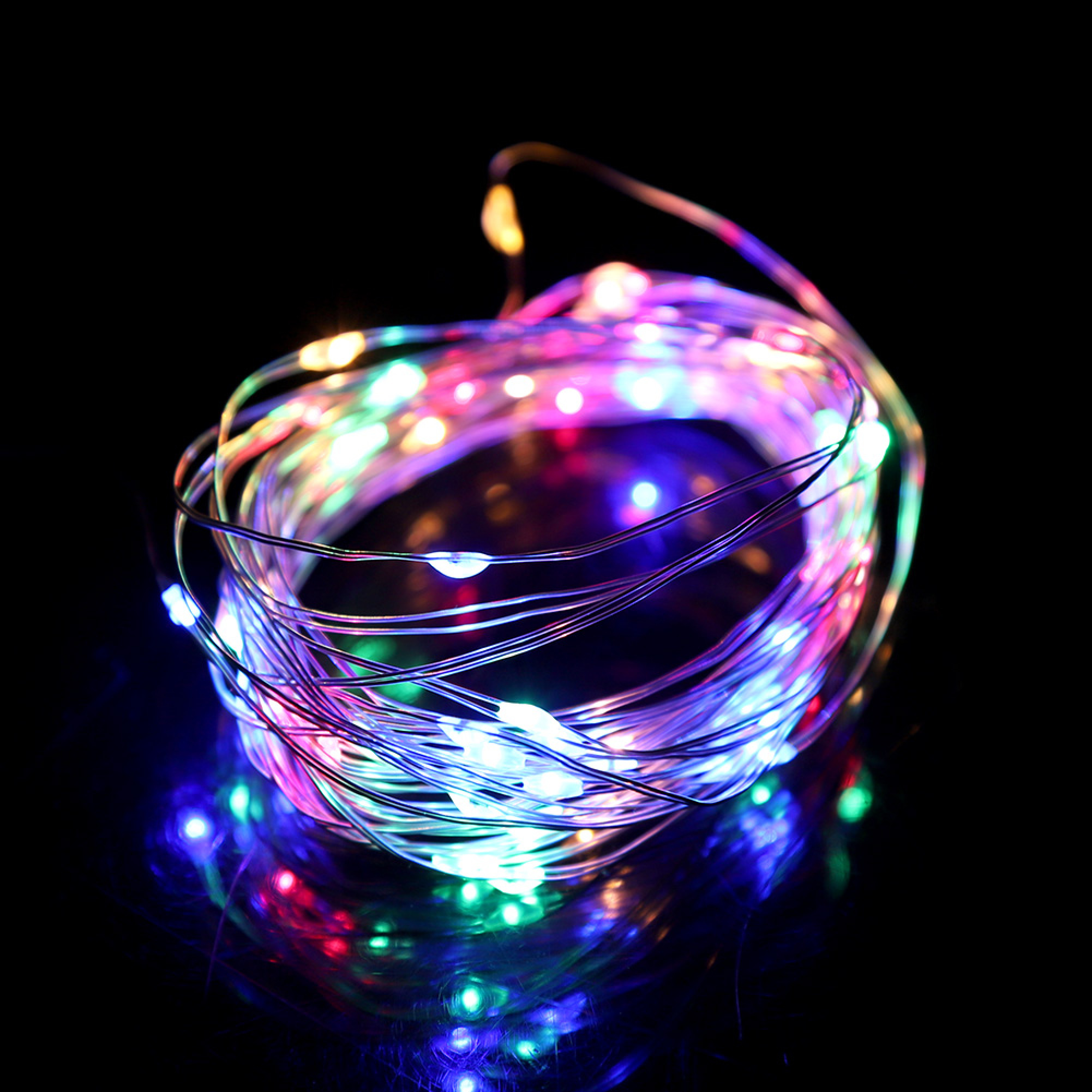 Eine aufgerollte Lichterkette mit bunten LEDs auf schwarzem Hintergrund.