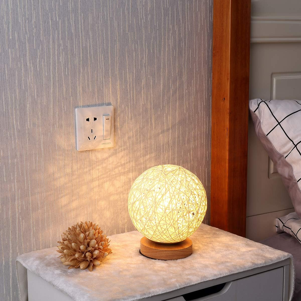 Eine runde Lampe aus Rattangeflecht steht auf einem Nachttisch neben einem Bett.