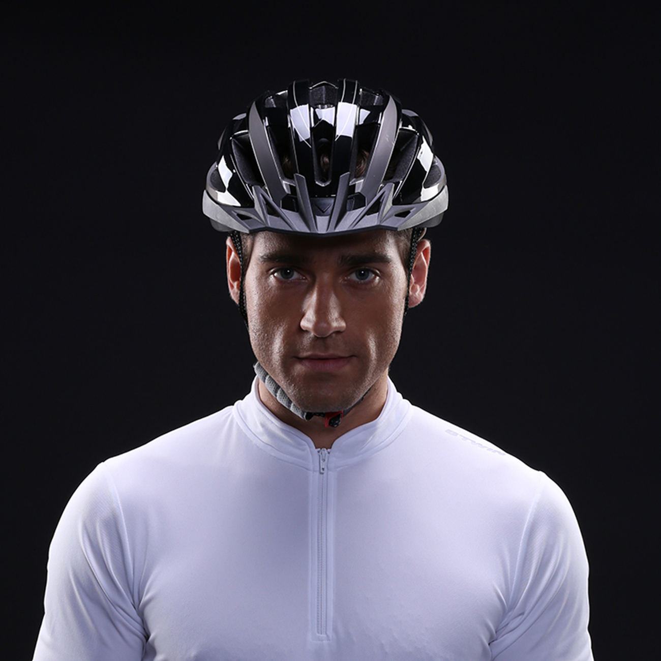Ein Mann trägt einen schwarzen Fahrradhelm und ein weißes Trikot vor schwarzem Hintergrund.