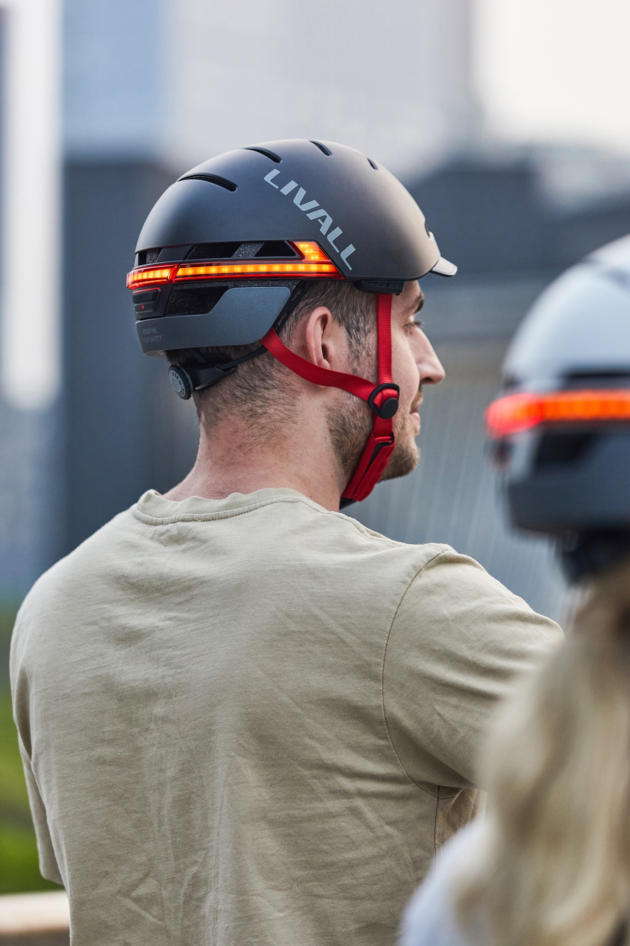 Mann in beige Hemd trägt schwarzen Helm mit roten Riemen und hinteren LED-Leuchten.