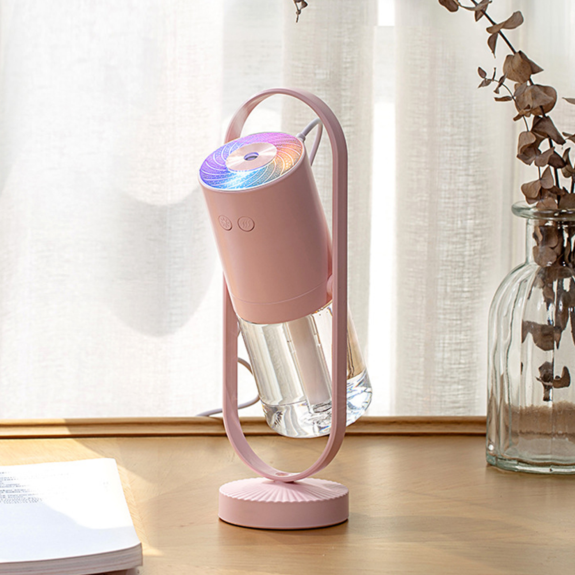 Ein rosa Luftbefeuchter mit buntem Licht steht auf einem Holzschreibtisch neben einer Glasvase.